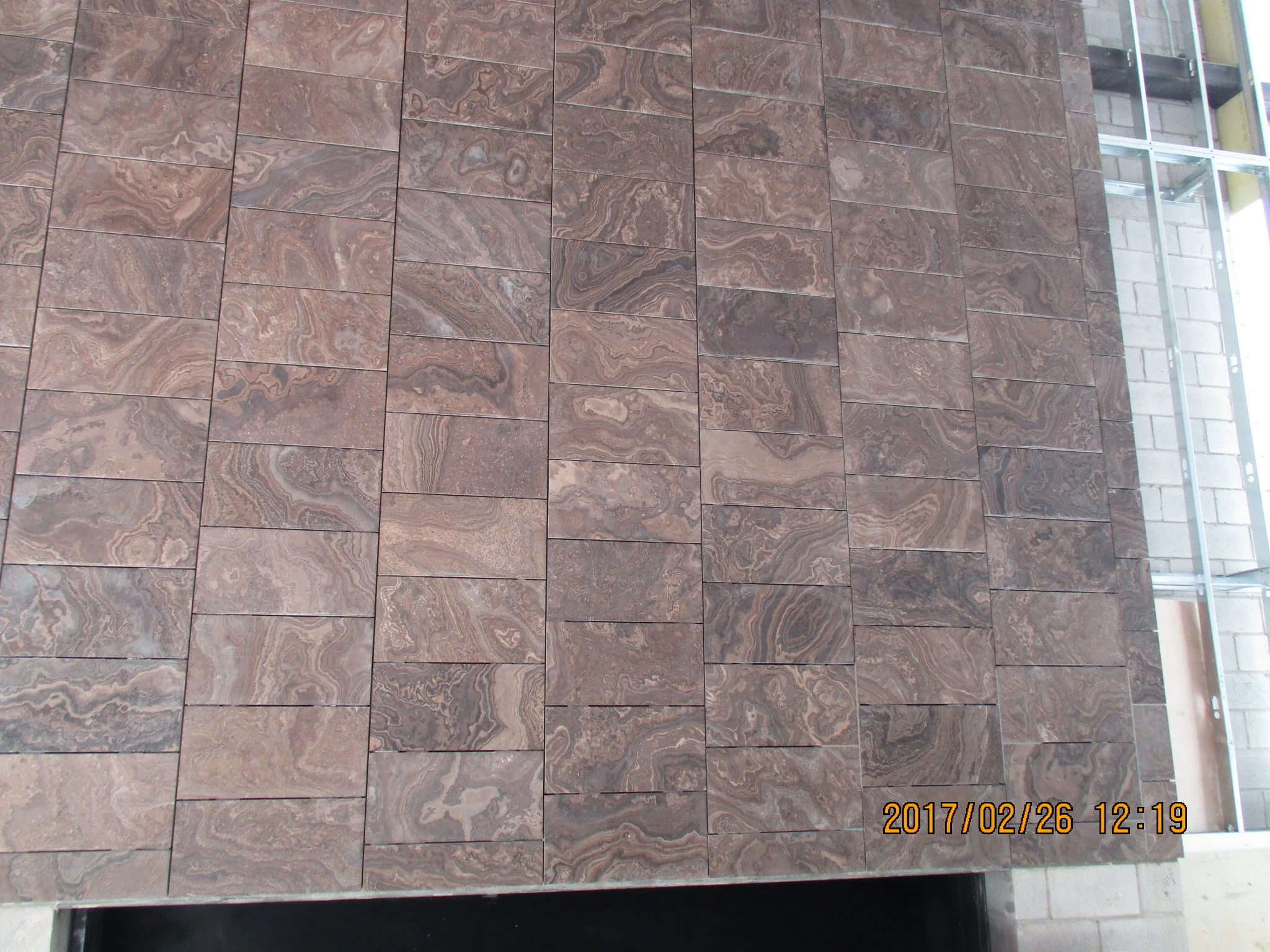 Close-up of a wall made of rectangular brown marble tiles with natural veining.