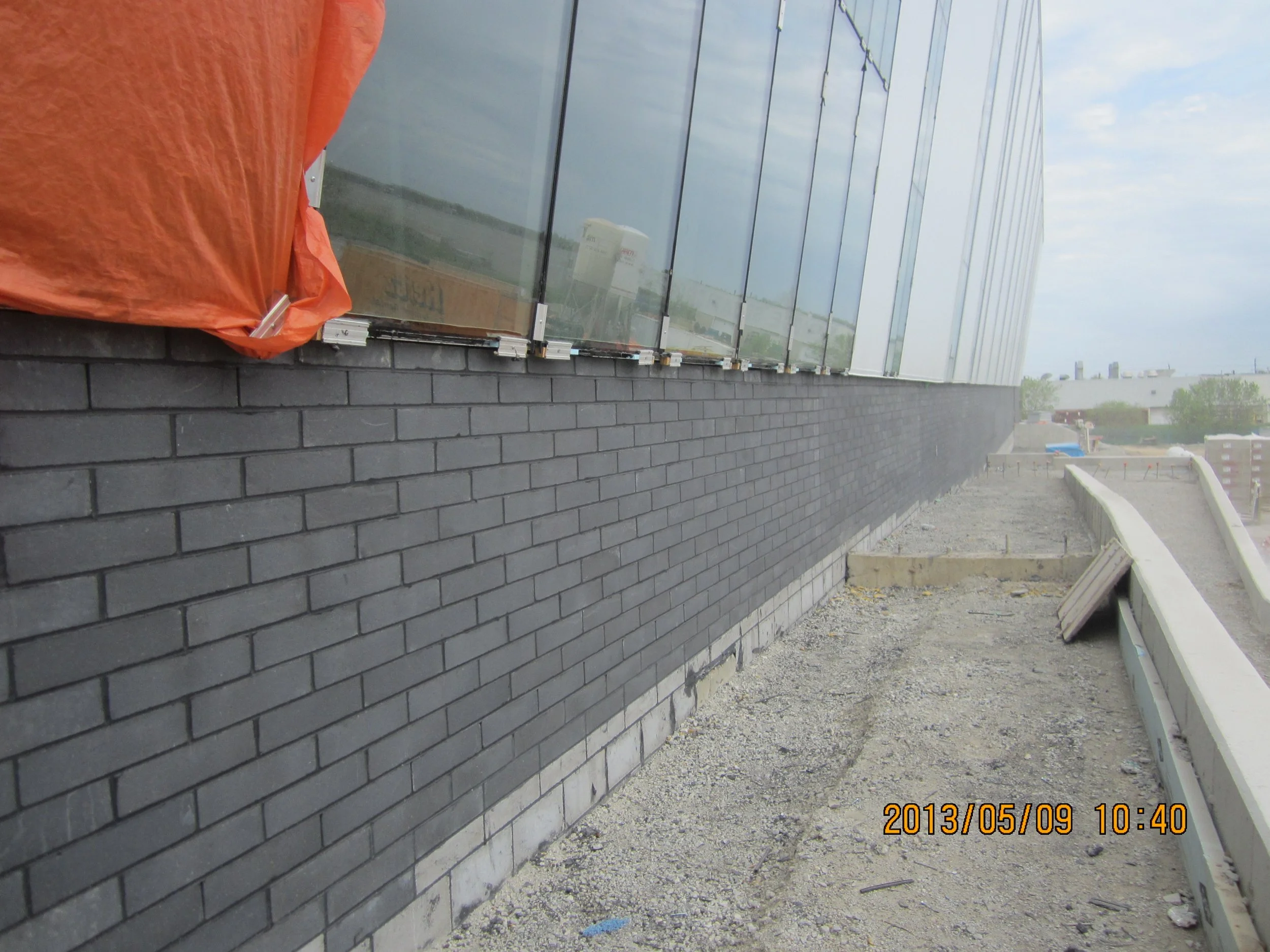 Construction site on a building rooftop with black brick walls, glass panels, and a white railing, overcast sky, and distant cityscape, timestamp on the photo reading 2013/05/09 10:40.