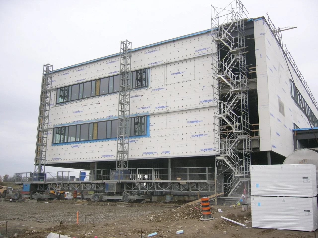 Construction site with a multi-story building under construction, featuring scaffolding along the side and wrapped exterior walls.