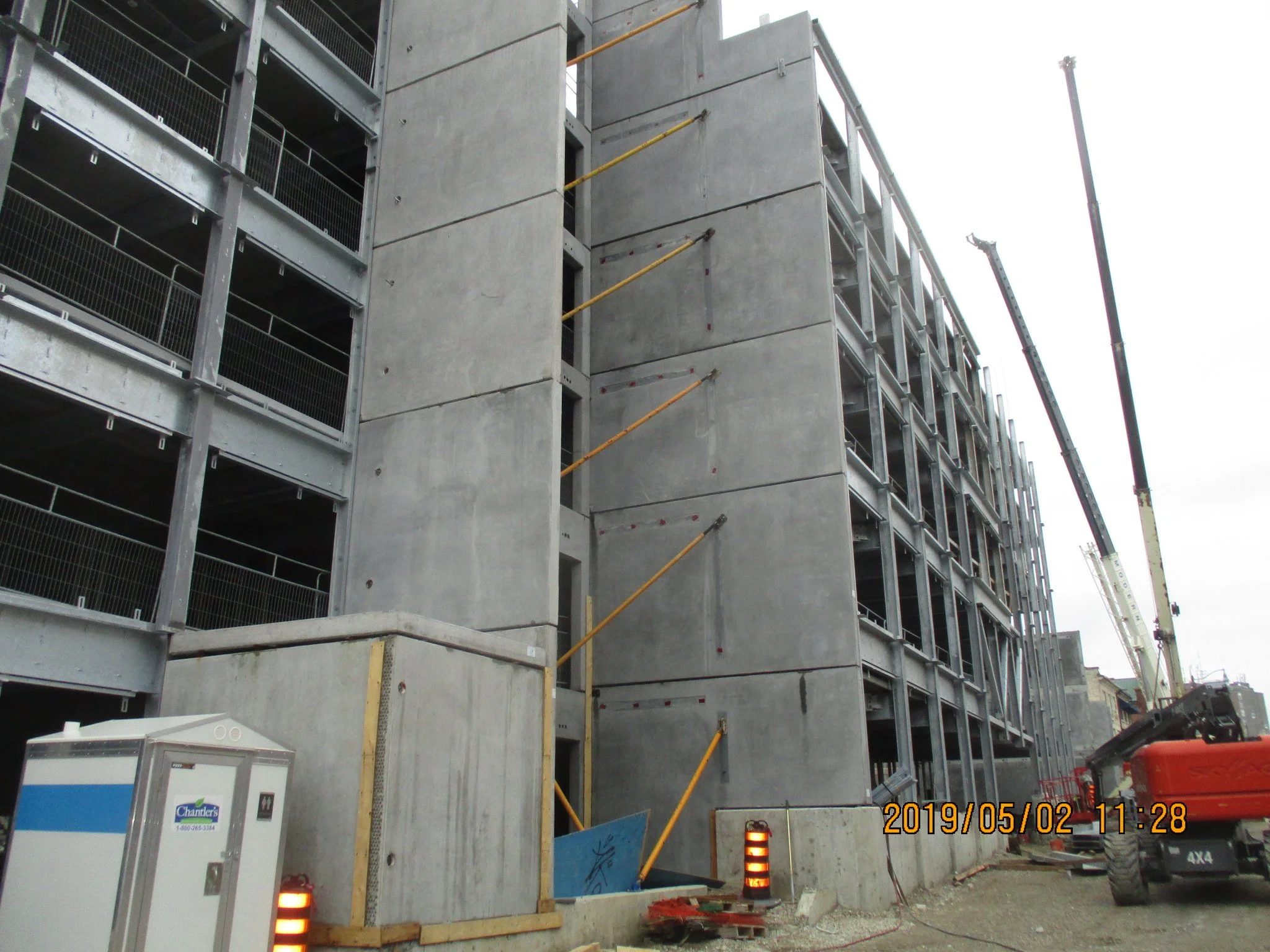 Construction site with a partially built multi-story concrete building, cranes, construction vehicles, and safety barriers.