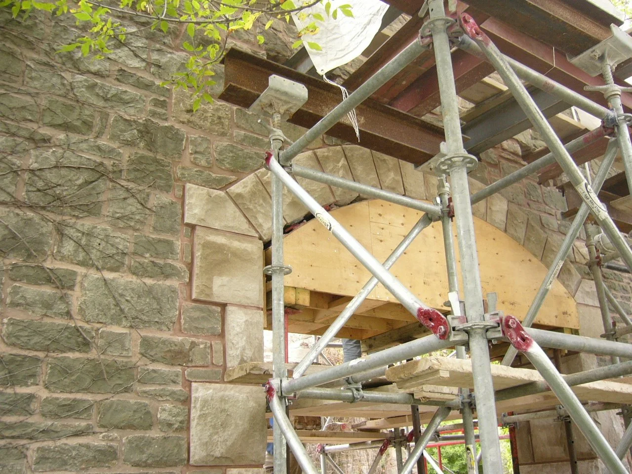 Construction scaffolding around a stone building showing an archway being repaired or restored.