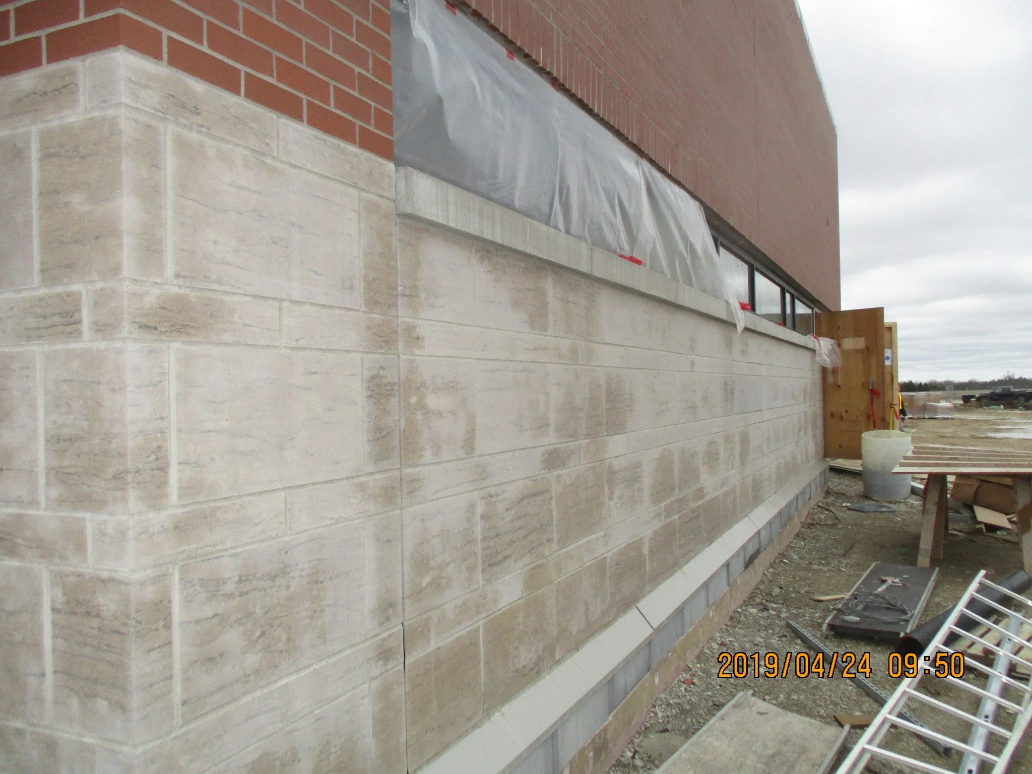 Construction site showing a building with brick and stone walls, with construction materials and tools scattered on the ground.