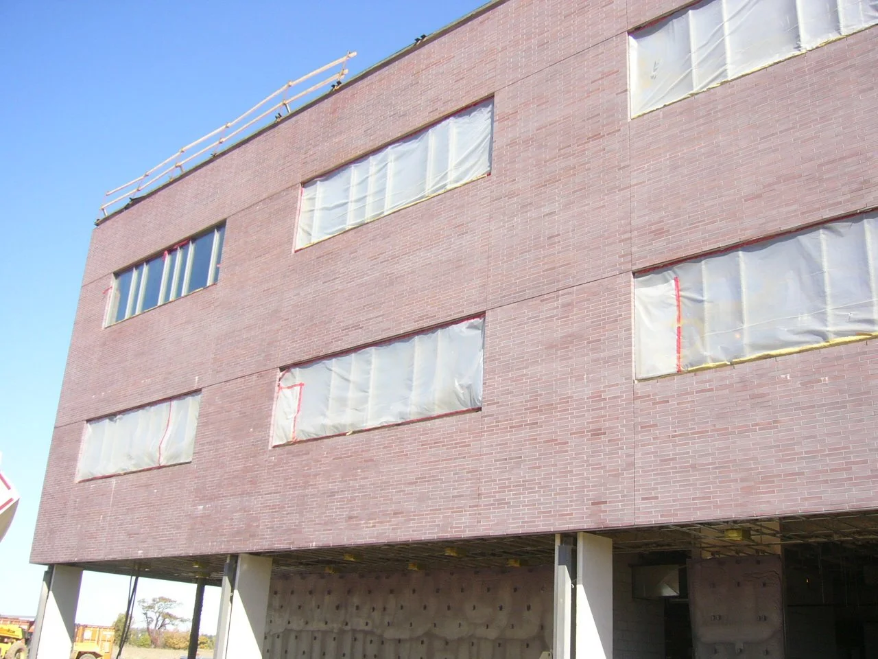 A multi-story building under construction with brick exterior and covered windows, supported by concrete pillars on the ground level.