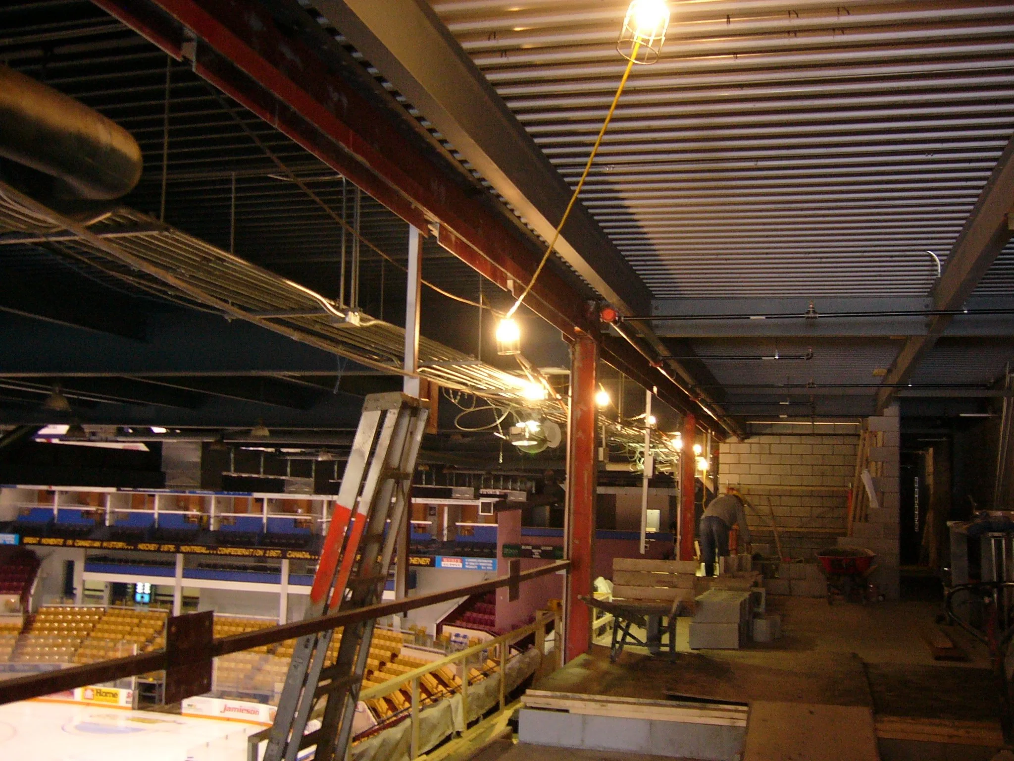 Interior view of a construction site in an arena or stadium, with scaffolding, ladders, and construction workers working on stairs.