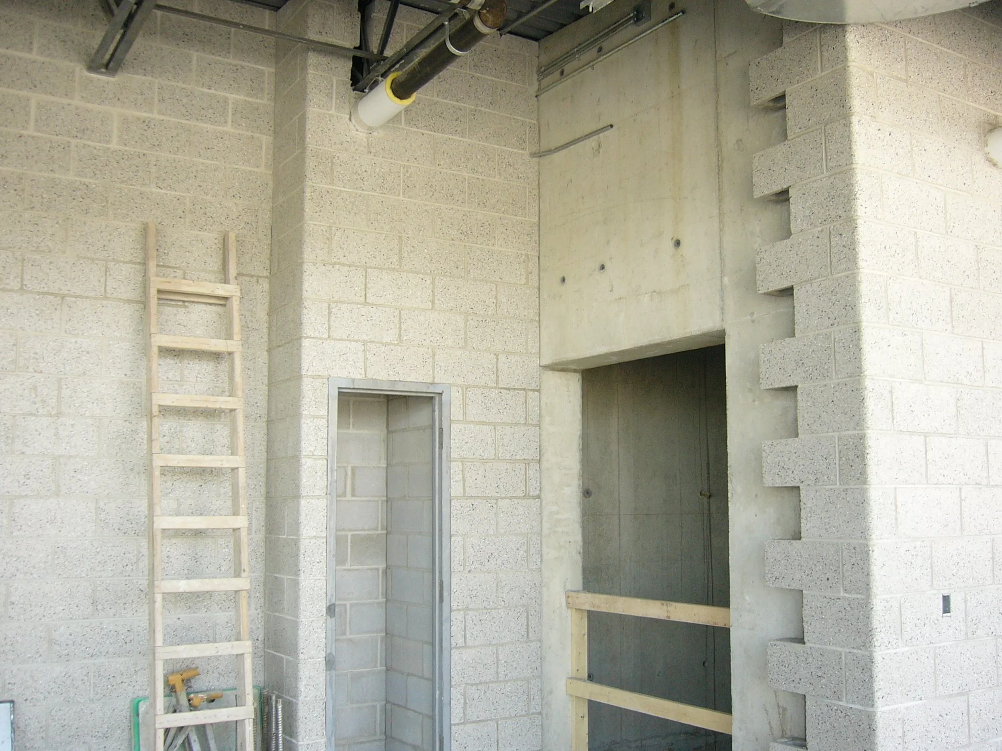Interior of a building under construction, showing brick walls, a wooden ladder, and various construction materials.