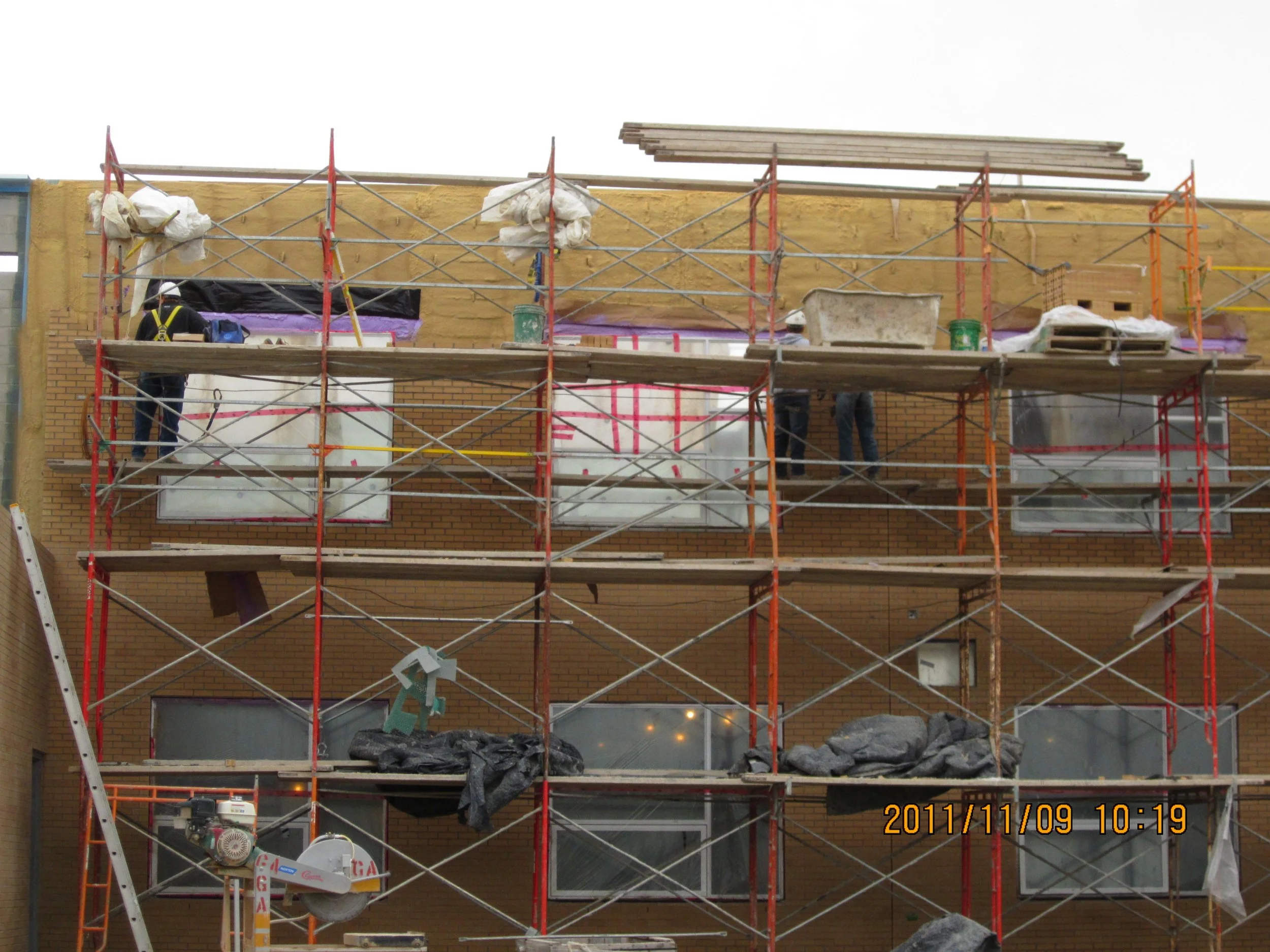 Construction workers on scaffolding working on the exterior wall of a building, with a brick facade, during daytime.
