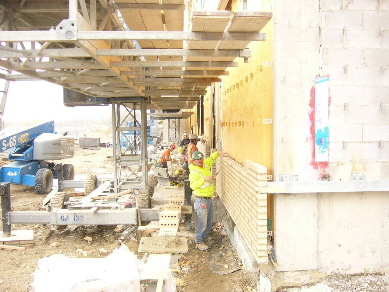 Construction workers building a brick wall on a building site with scaffolding and construction equipment.