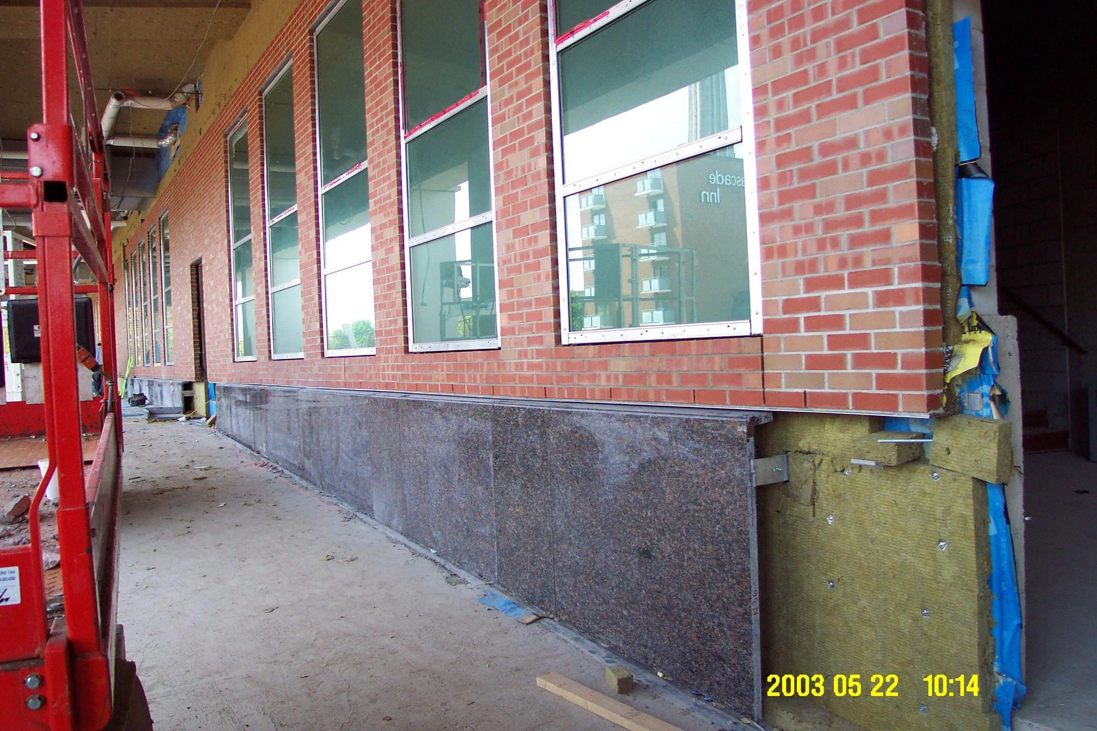 Building under construction with brick walls, multiple large windows, and a granite foundation. Construction materials and scaffolding visible.