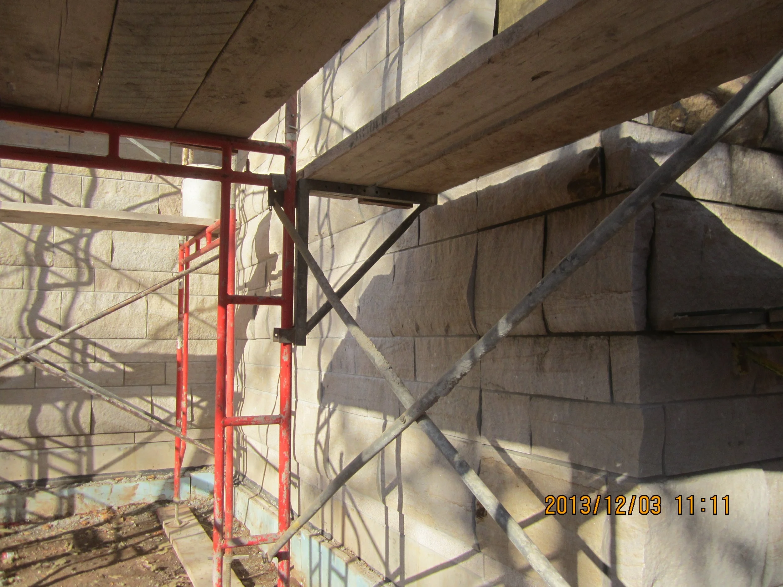 Scaffolding set up next to a stone wall with sunlight casting shadows on it. The photo was taken on December 3, 2013, at 11:11 am.