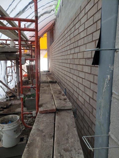View of a construction site showing scaffolding, a brick wall, and building materials on the ground.