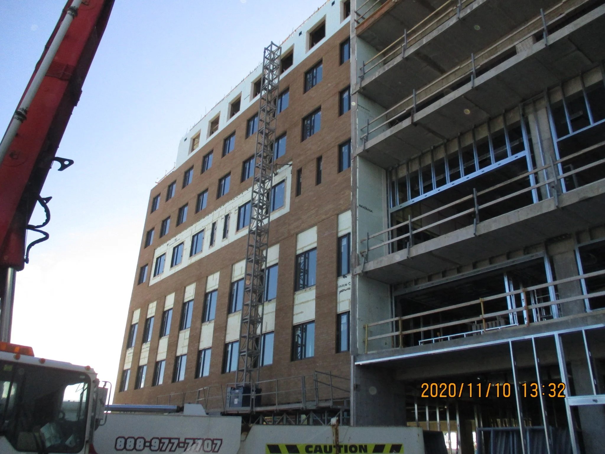 Construction of a multi-story building with brown brick exterior, steel scaffolding, and some windows installed.