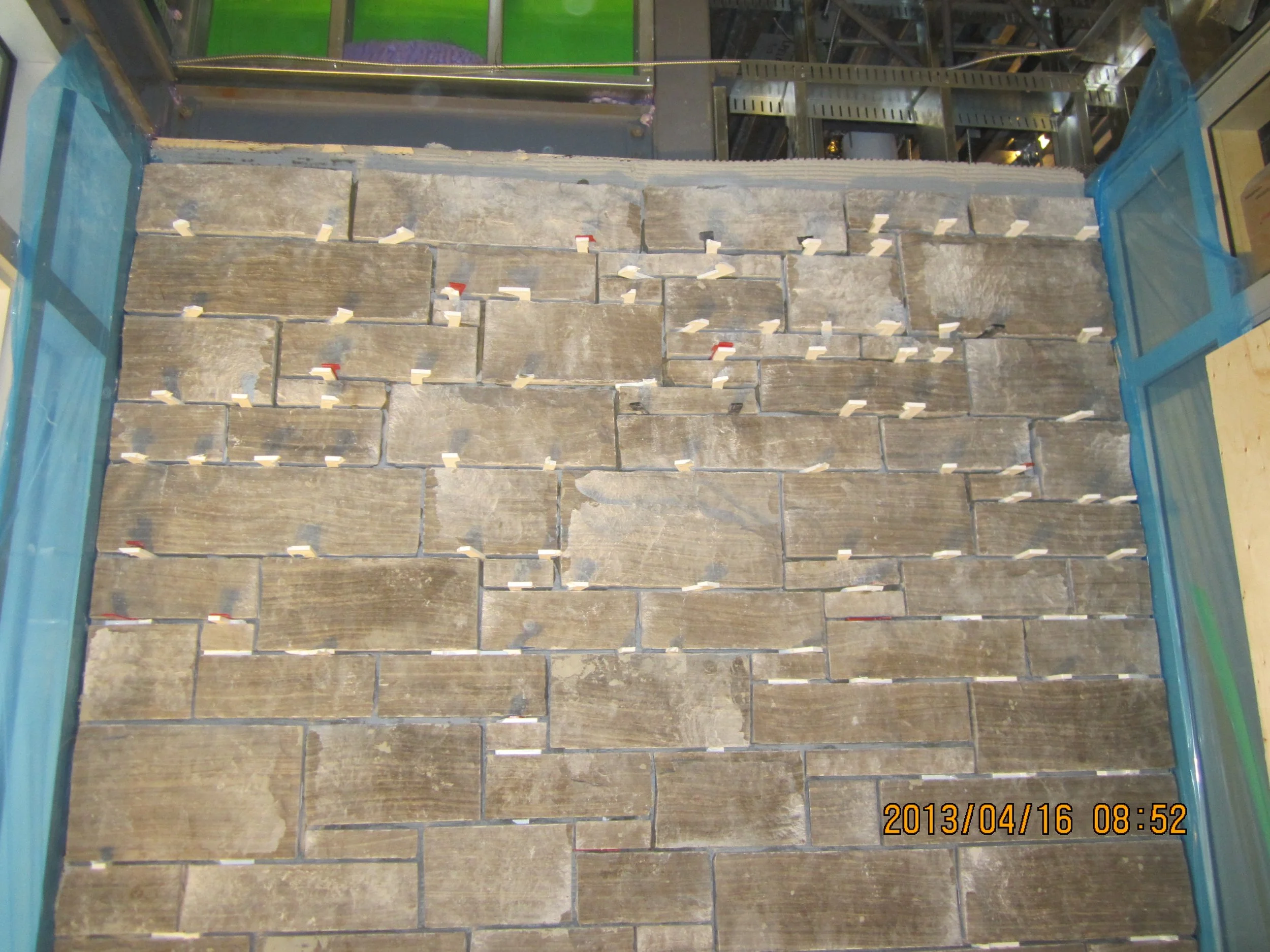Display of stone tiles arranged in a pattern, with small white labels attached to many of them, enclosed by blue framing on both sides.