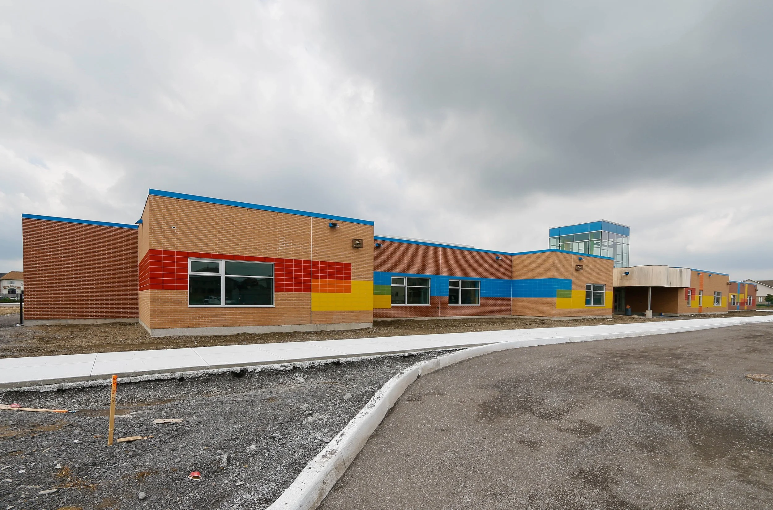 A colorful modern building, possibly a school or community center, with blue, red, yellow, and green accents, under a cloudy sky.