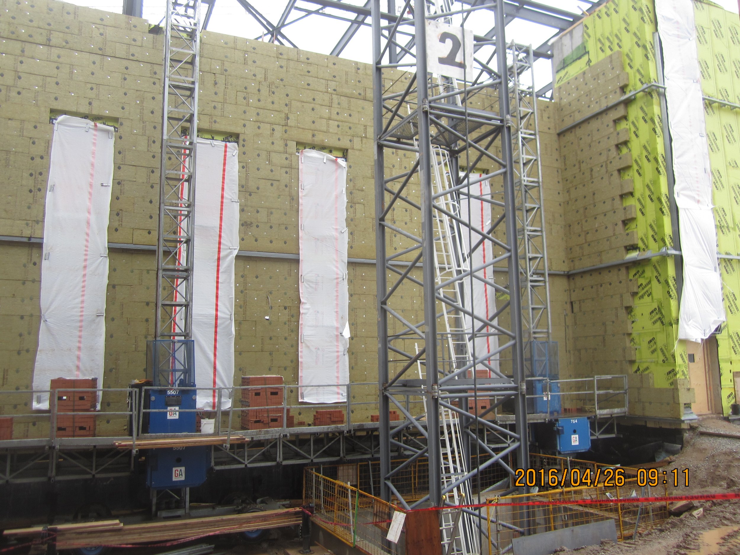 Construction site with a partially built building, scaffolding, and insulation materials on the walls.
