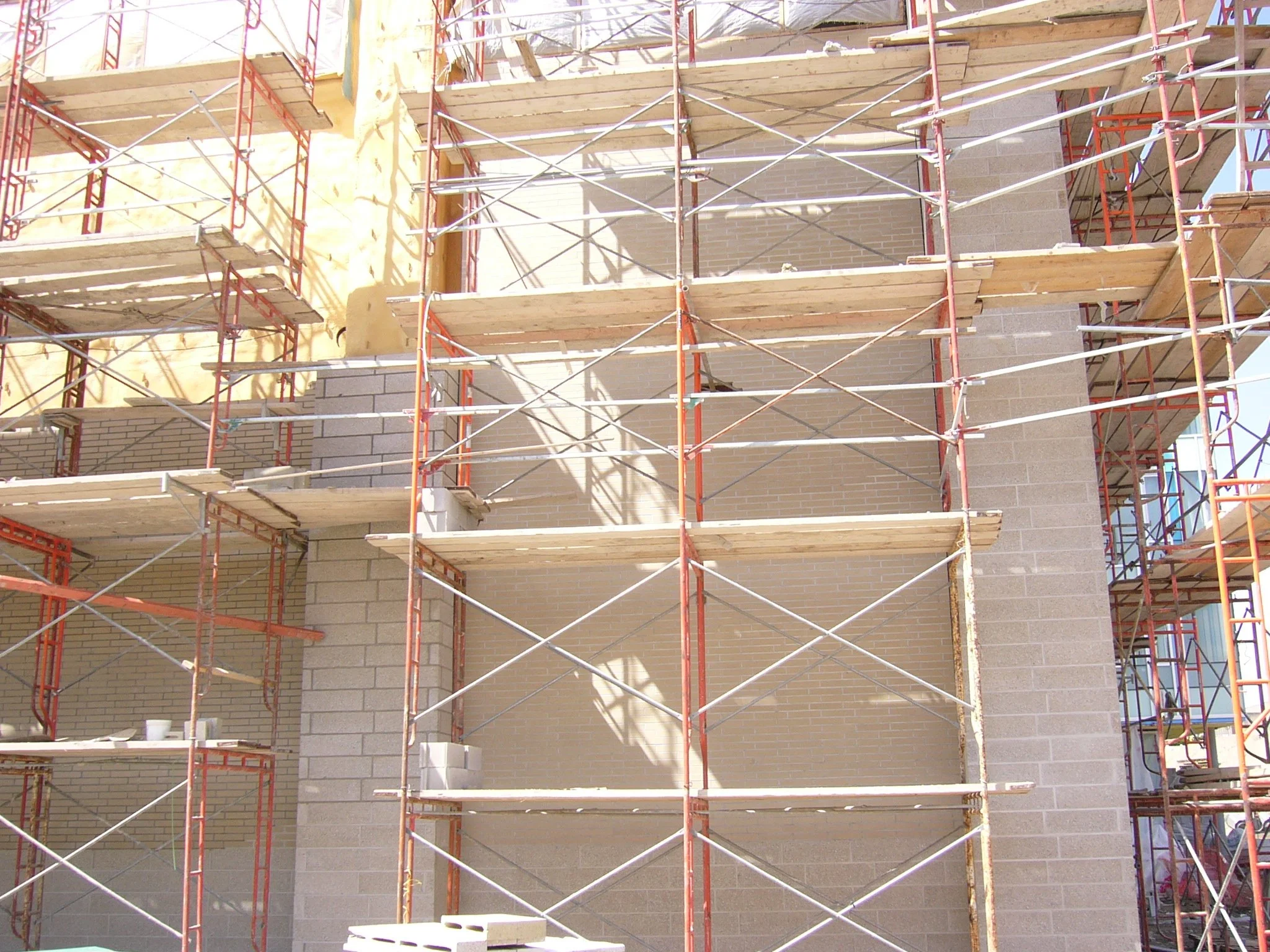 Construction scaffolding set up around a building under construction, with bricks and concrete visible.