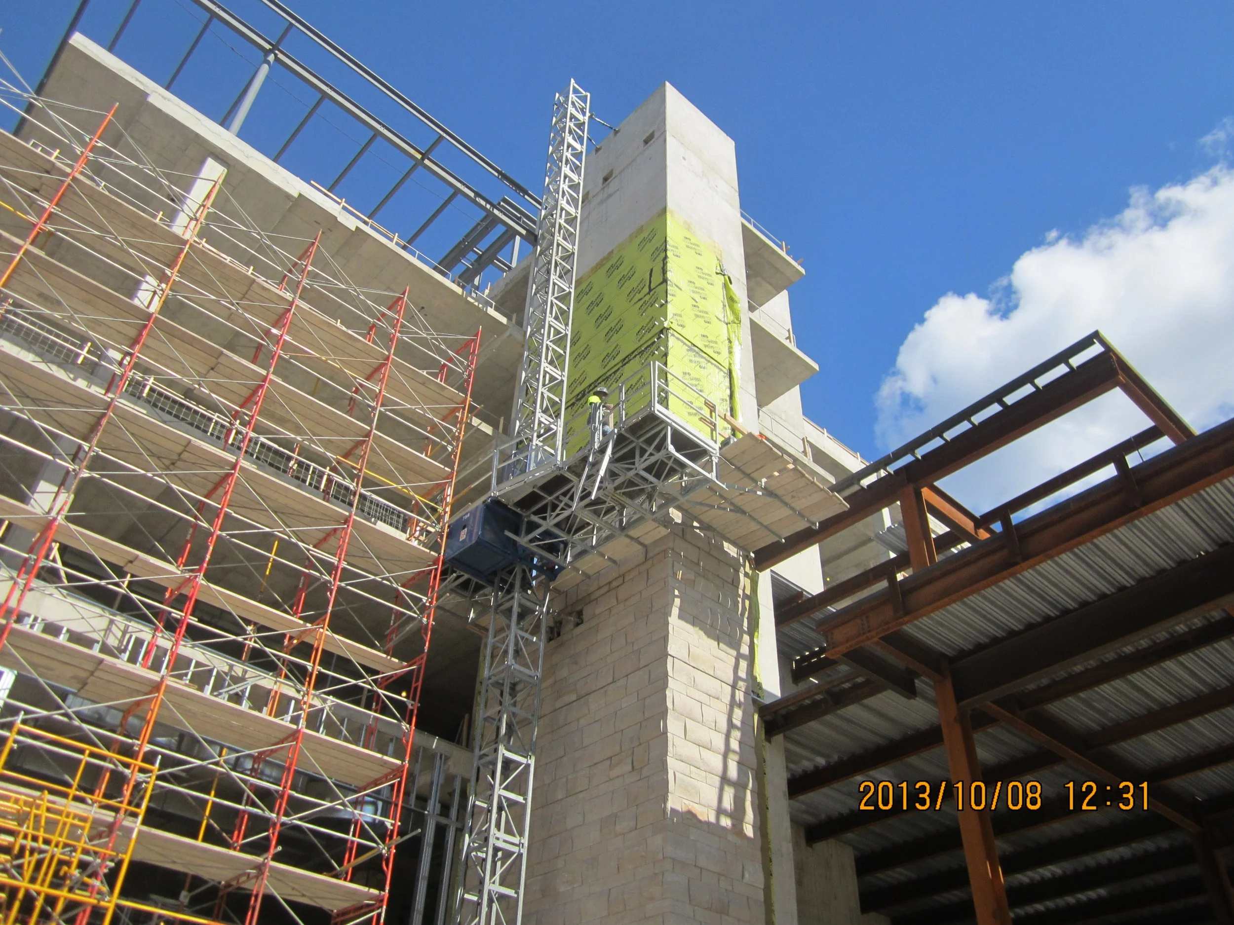 Construction site with scaffolding and a tower crane building a high-rise structure under a partly cloudy sky.
