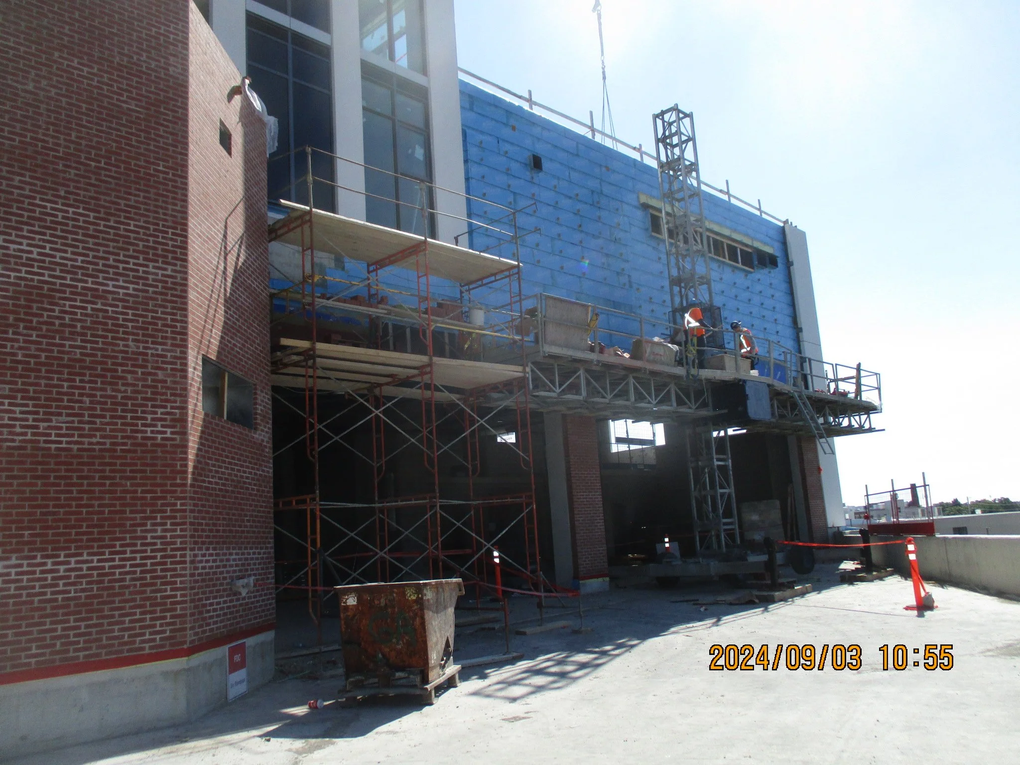 Construction workers working on a building exterior with scaffolding, brick and blue siding, under clear sky on a bright day.