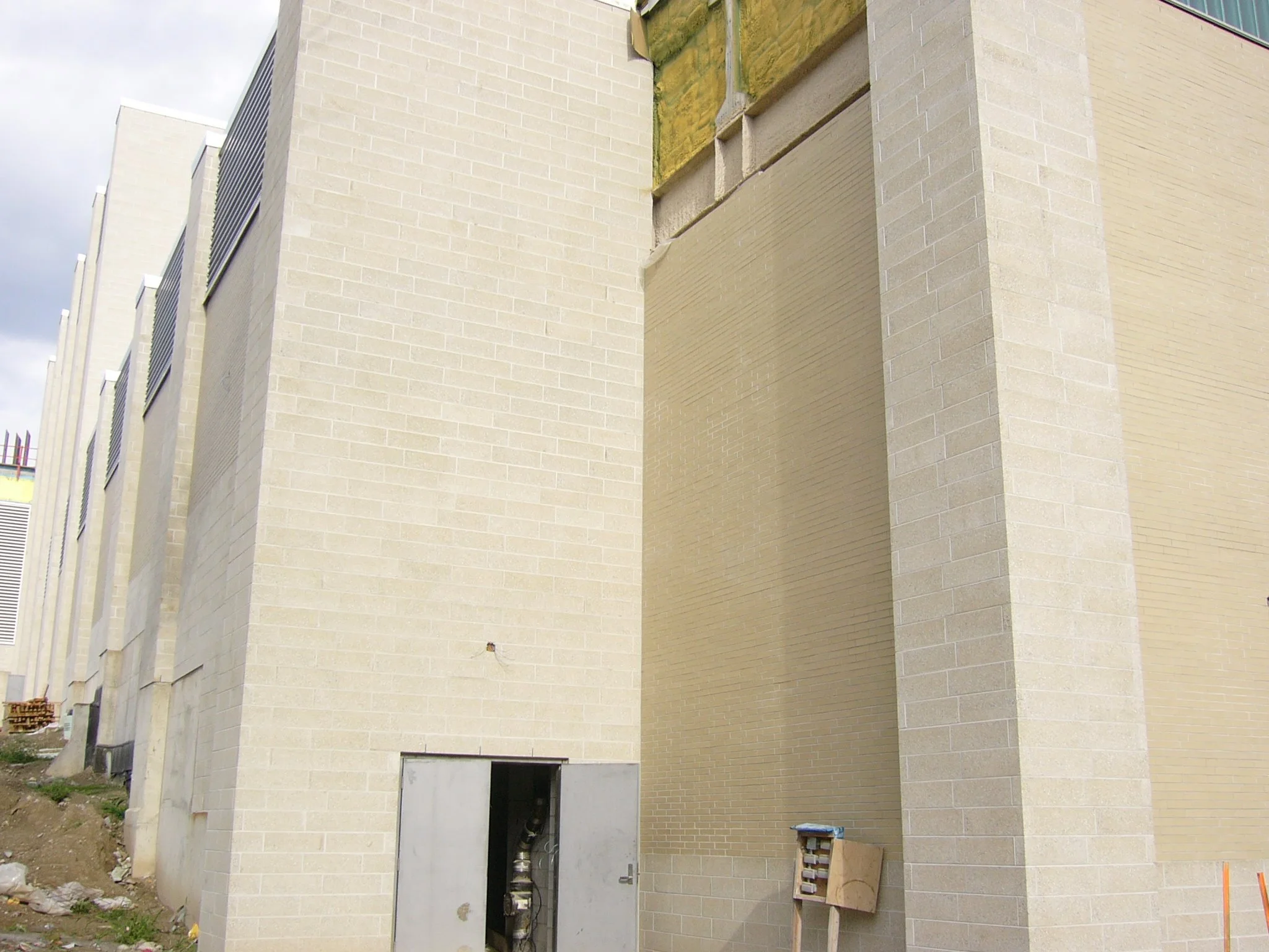 Close-up of a construction site showing beige brick walls of a building with some sections unfinished and construction materials on the ground.