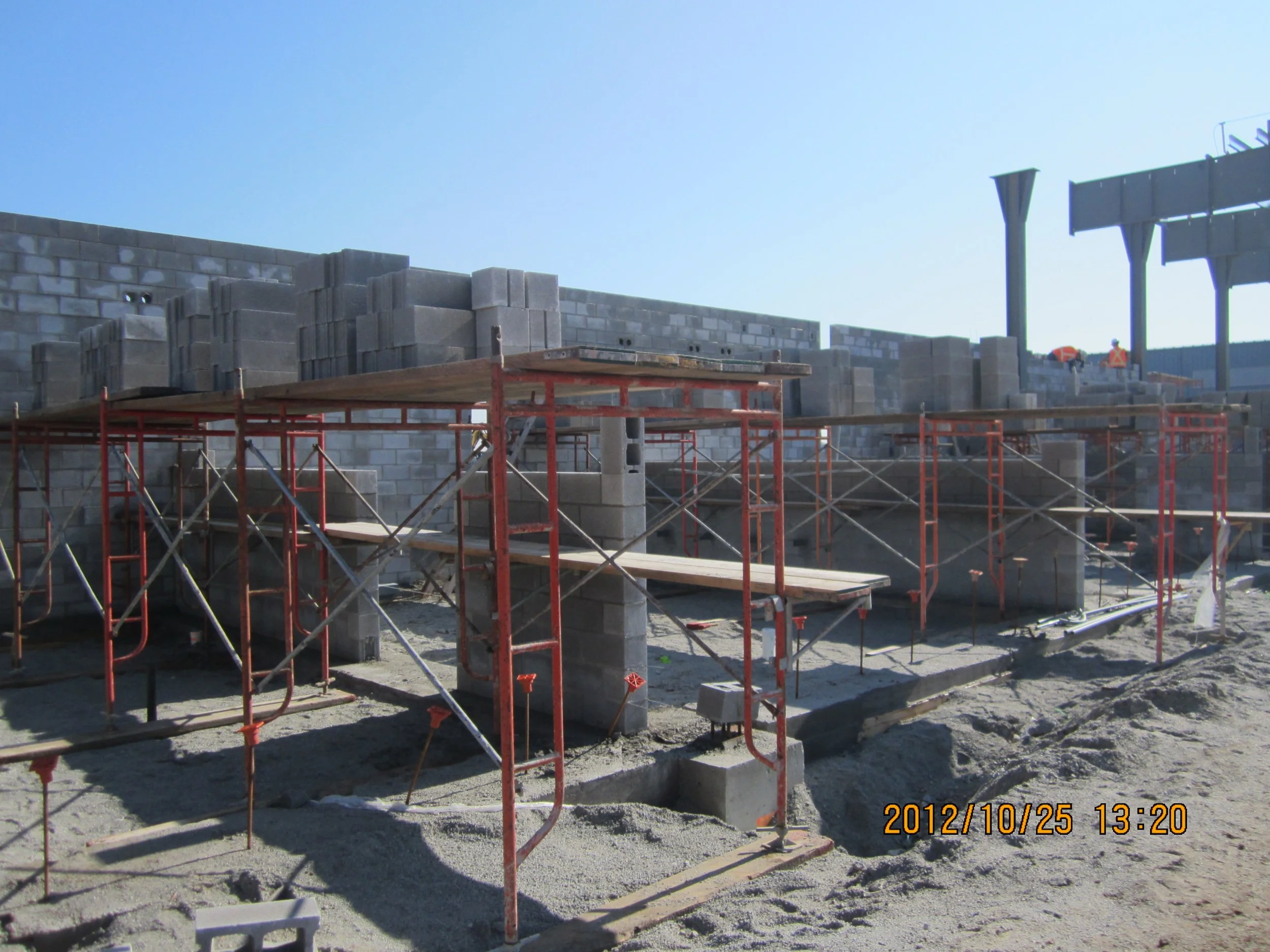 Construction site with scaffolding, grey cinder block wall under construction, and workers in safety vests in the background.