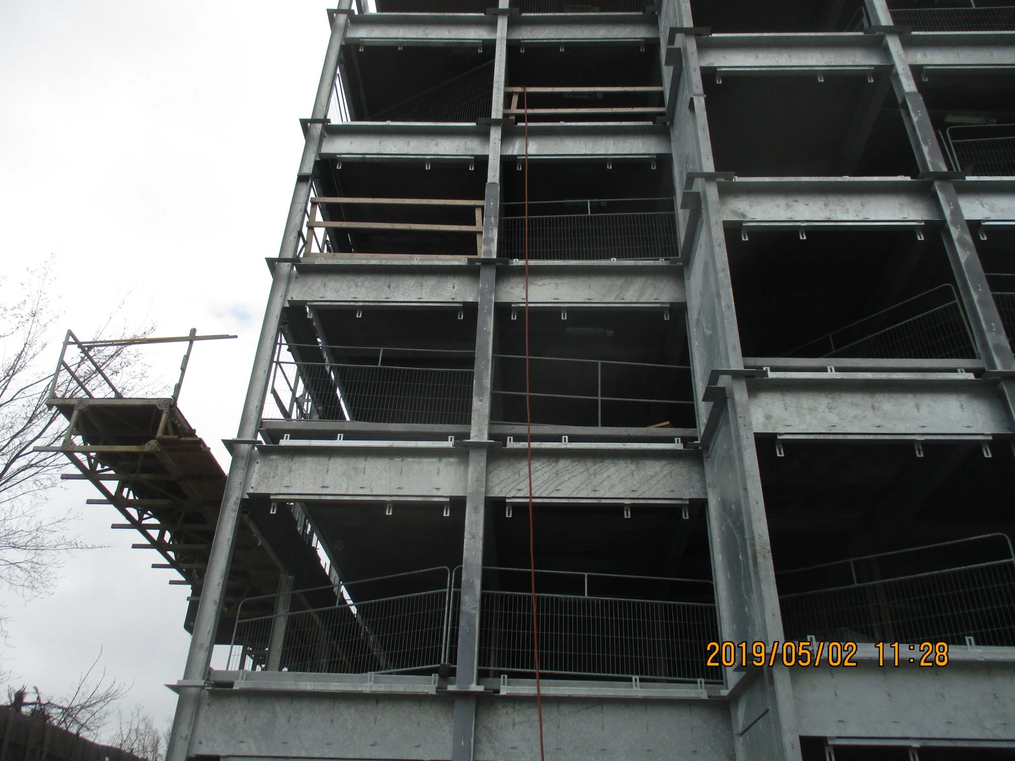 A multi-story building under construction, with visible steel framework and unfinished floors, against a cloudy sky.
