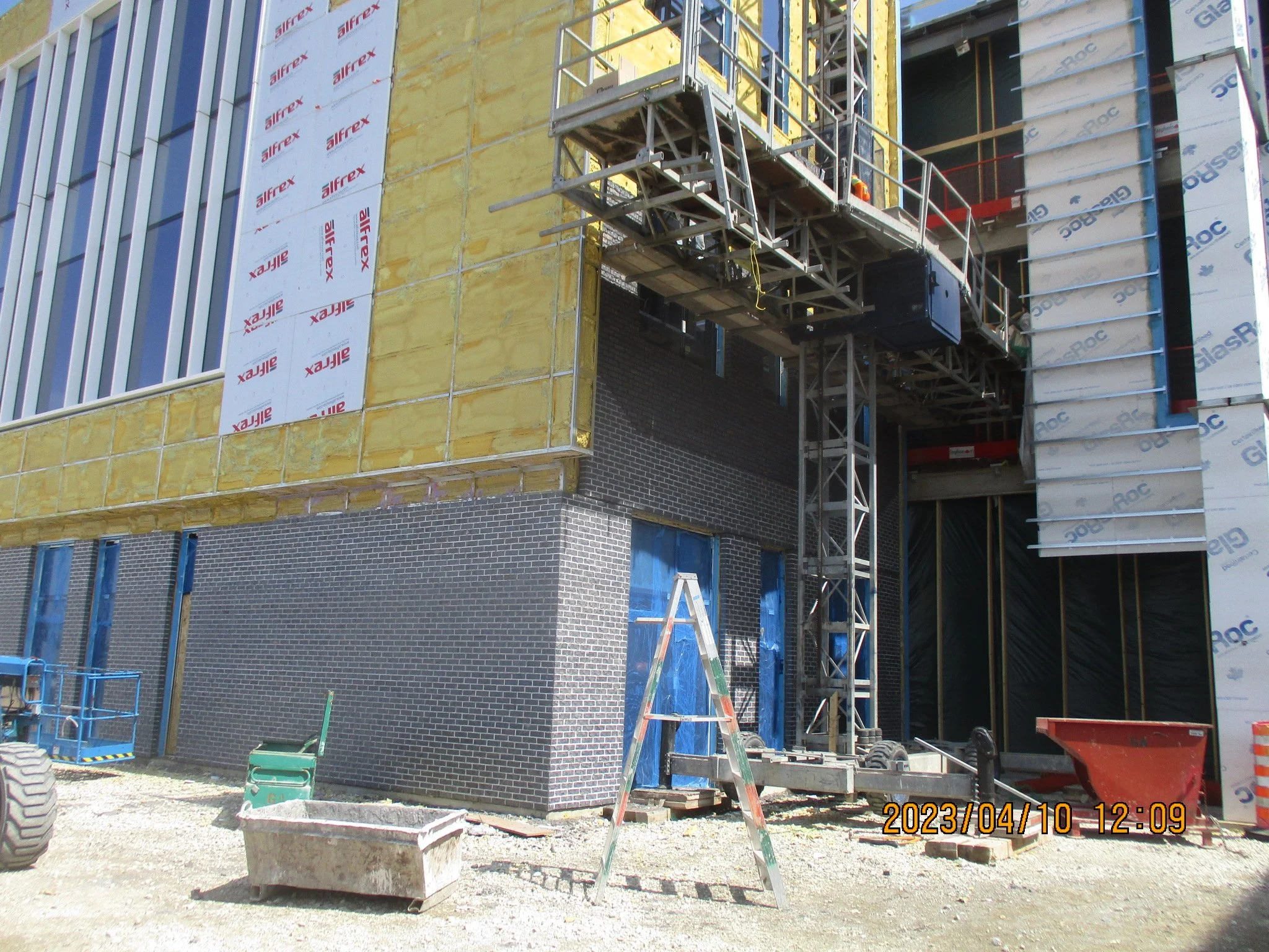 Construction site with scaffolding, a ladder, and building materials. Part of the building facade is under construction, showing insulation and brickwork.