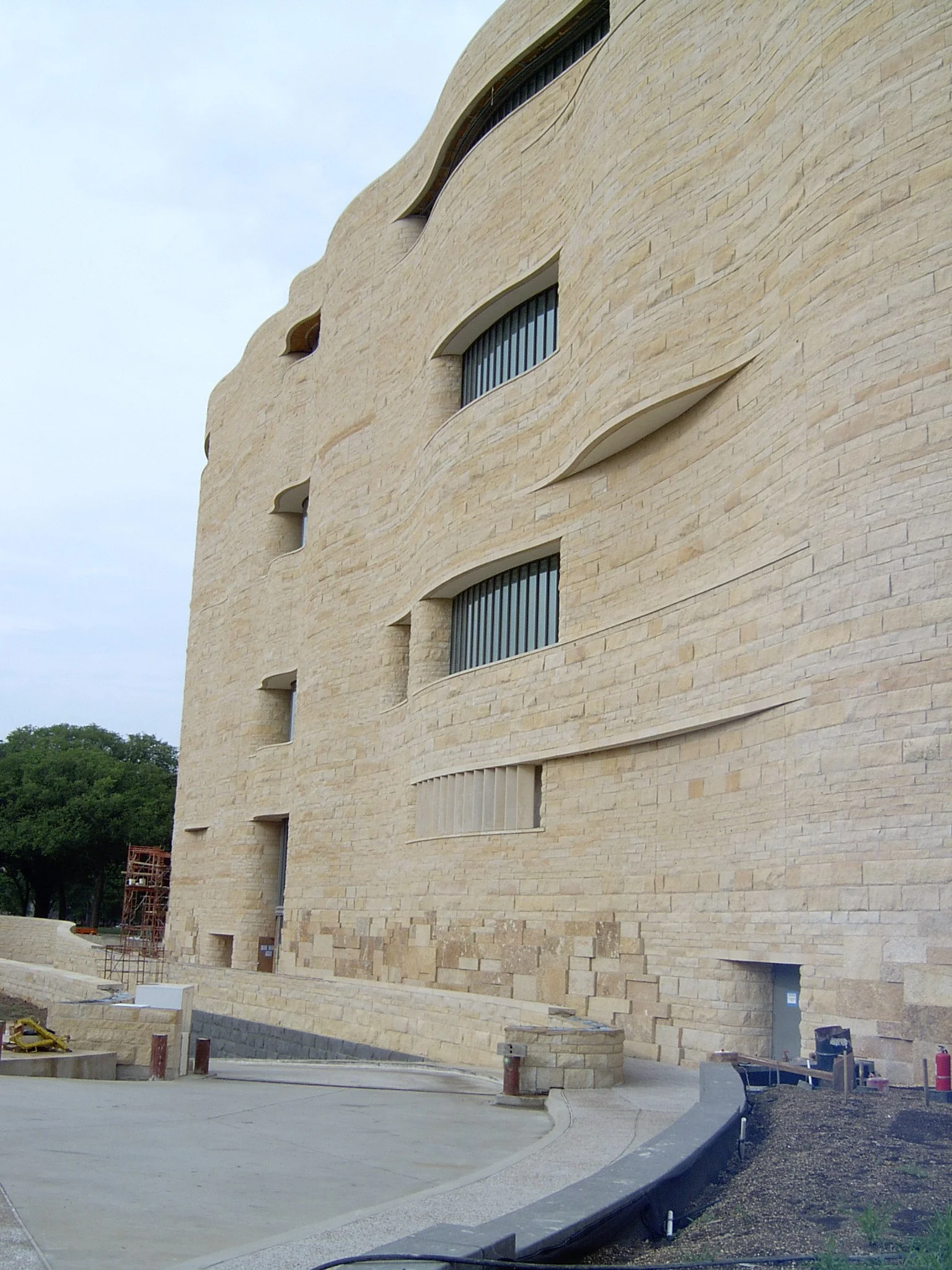 A modern beige stone building with curved architectural design and narrow horizontal windows, under construction.
