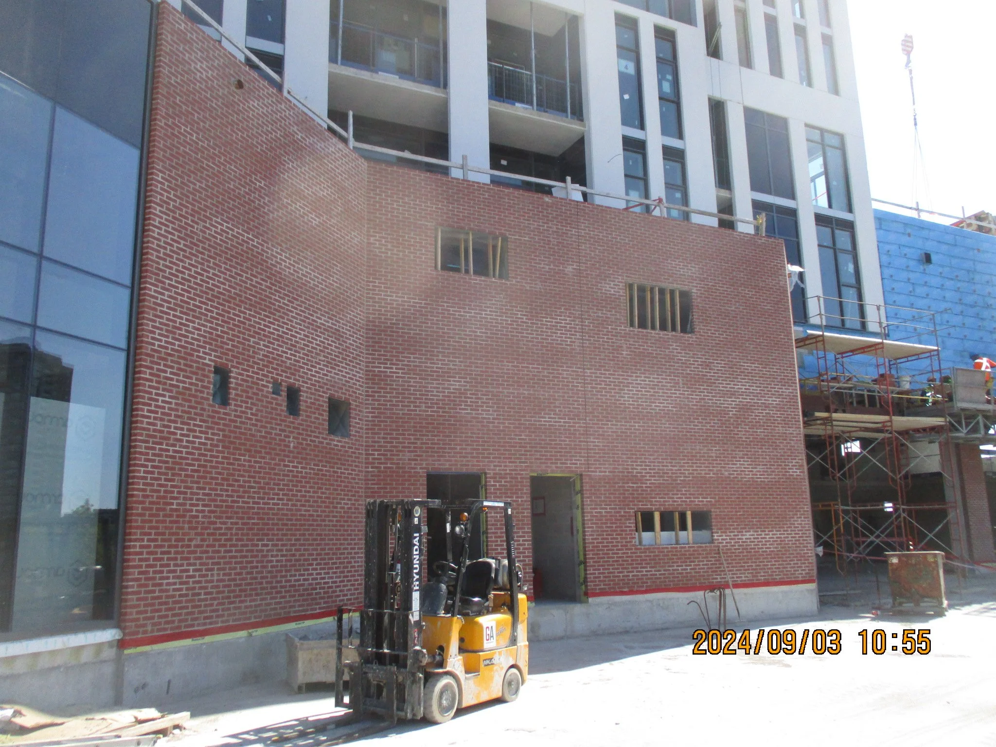 Construction site with a partially built brick wall, a yellow forklift in front, and scaffolding on the right side. The building has large windows and the date and time stamp shows September 3, 2024, at 10:55.