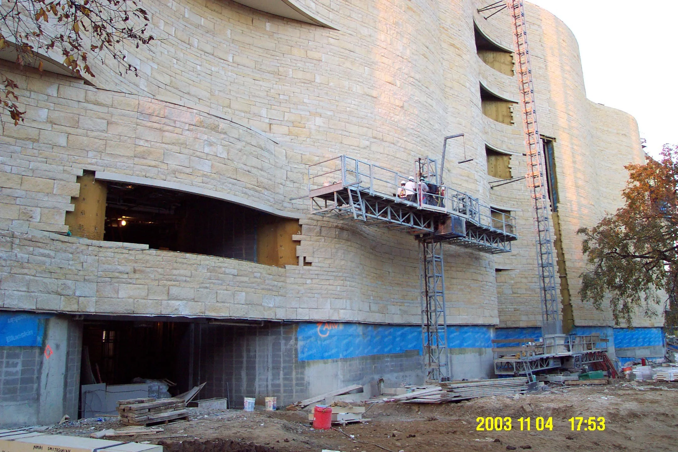 Construction site of a large building with scaffolding and workers installing the exterior stone facade.