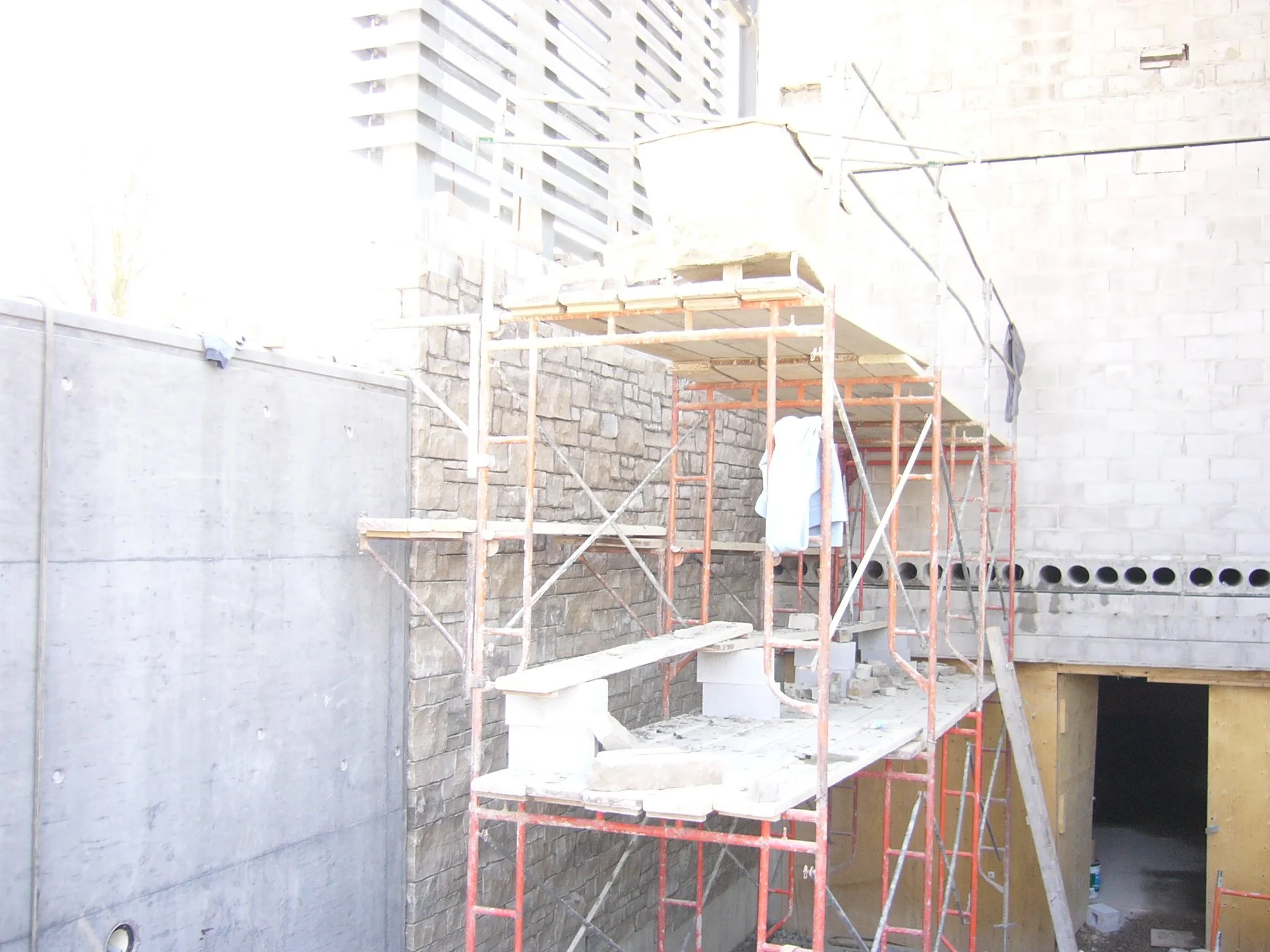 Construction scaffolding and building materials at a construction site with a partially built brick wall and an unfinished opening in the wall.