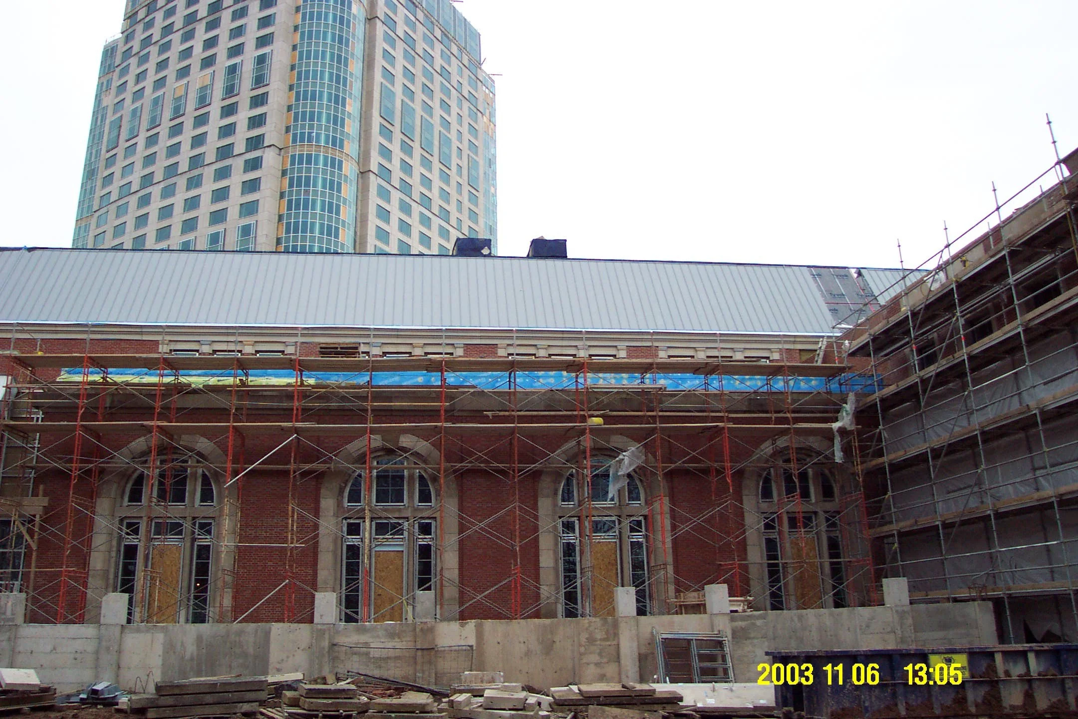 Construction site with scaffolding and building in progress, with a modern high-rise building in the background.
