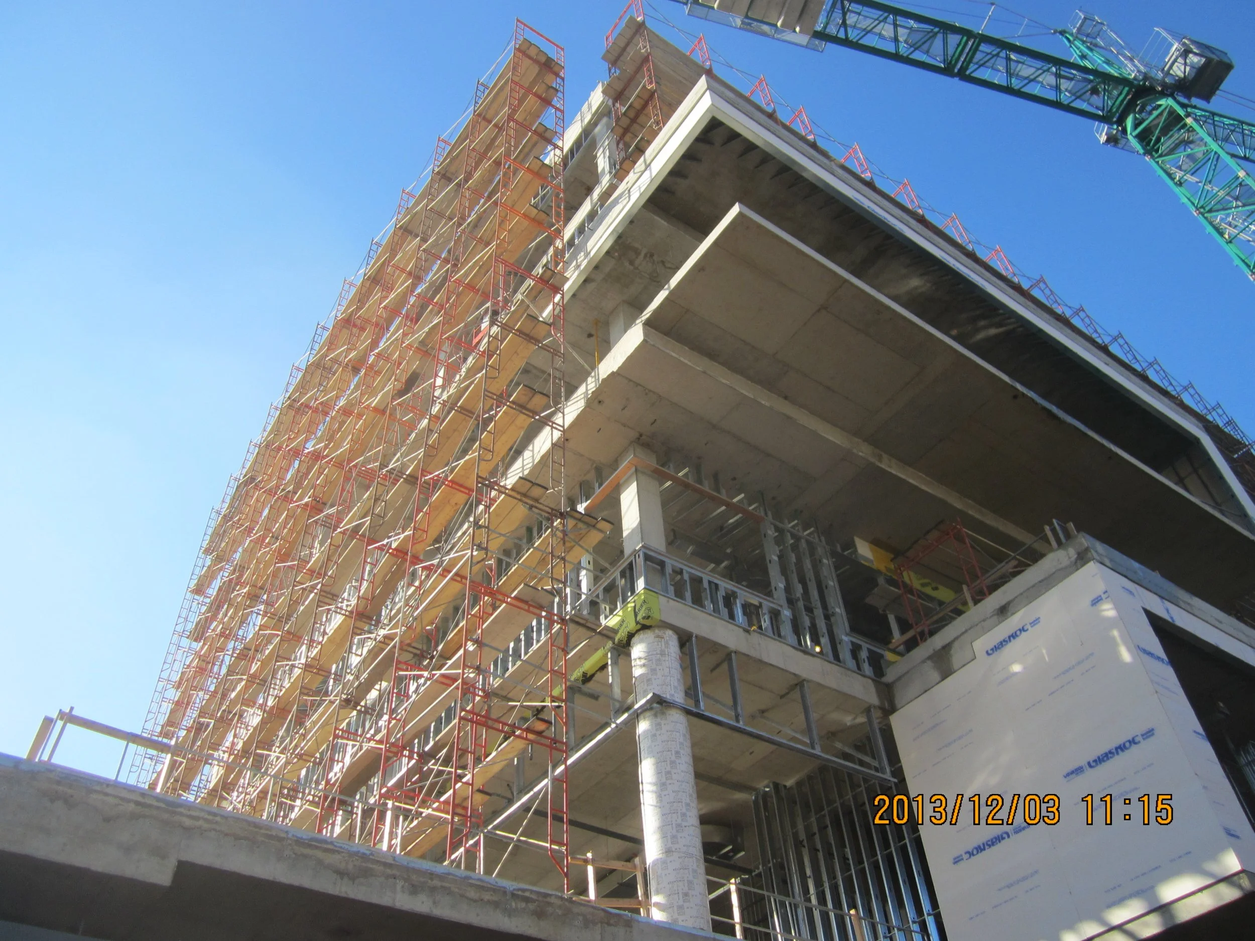Construction site with scaffolding and partially built concrete structure, high-rise building under construction, blue sky, and a green crane.