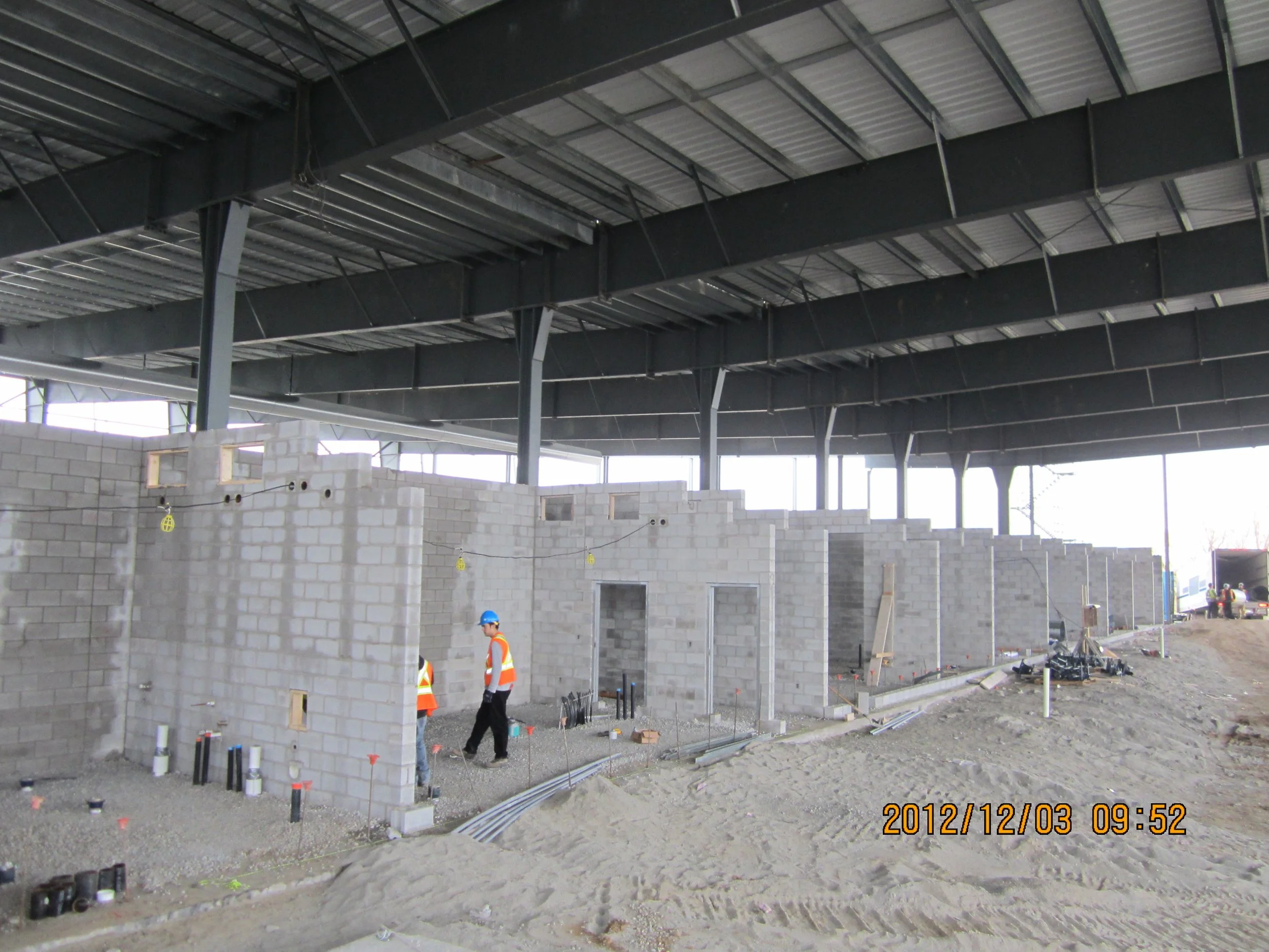 Construction site with unfinished concrete block walls and two workers in safety vests and helmets.