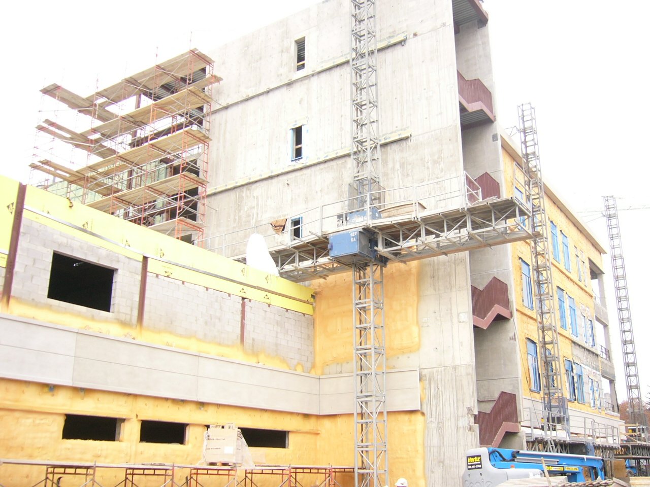 Construction site with a multi-story building under construction, scaffolding, and a tower crane.