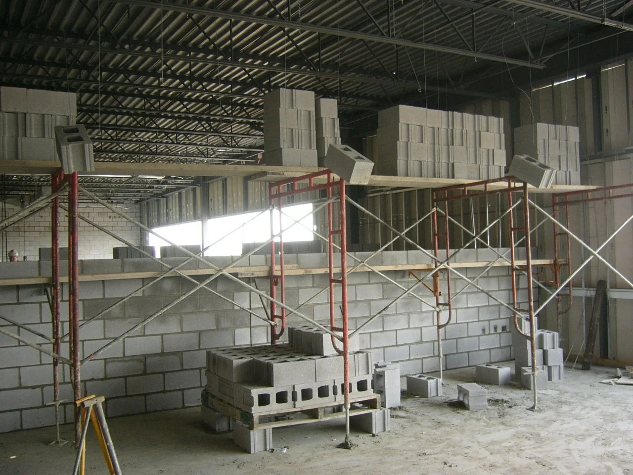 Construction site with brick walls, scaffolding, and concrete blocks stacked on a floor and on a platform inside a building under construction.