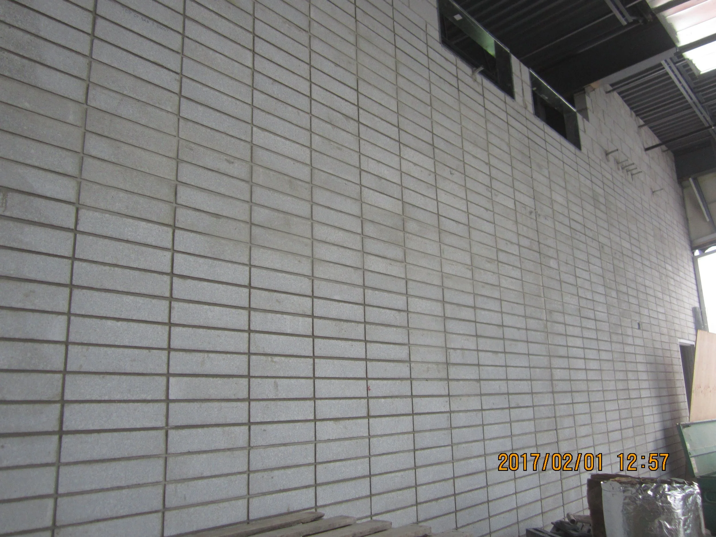 A tall beige brick wall under construction or renovation with square bricks and some construction materials at the bottom right corner.