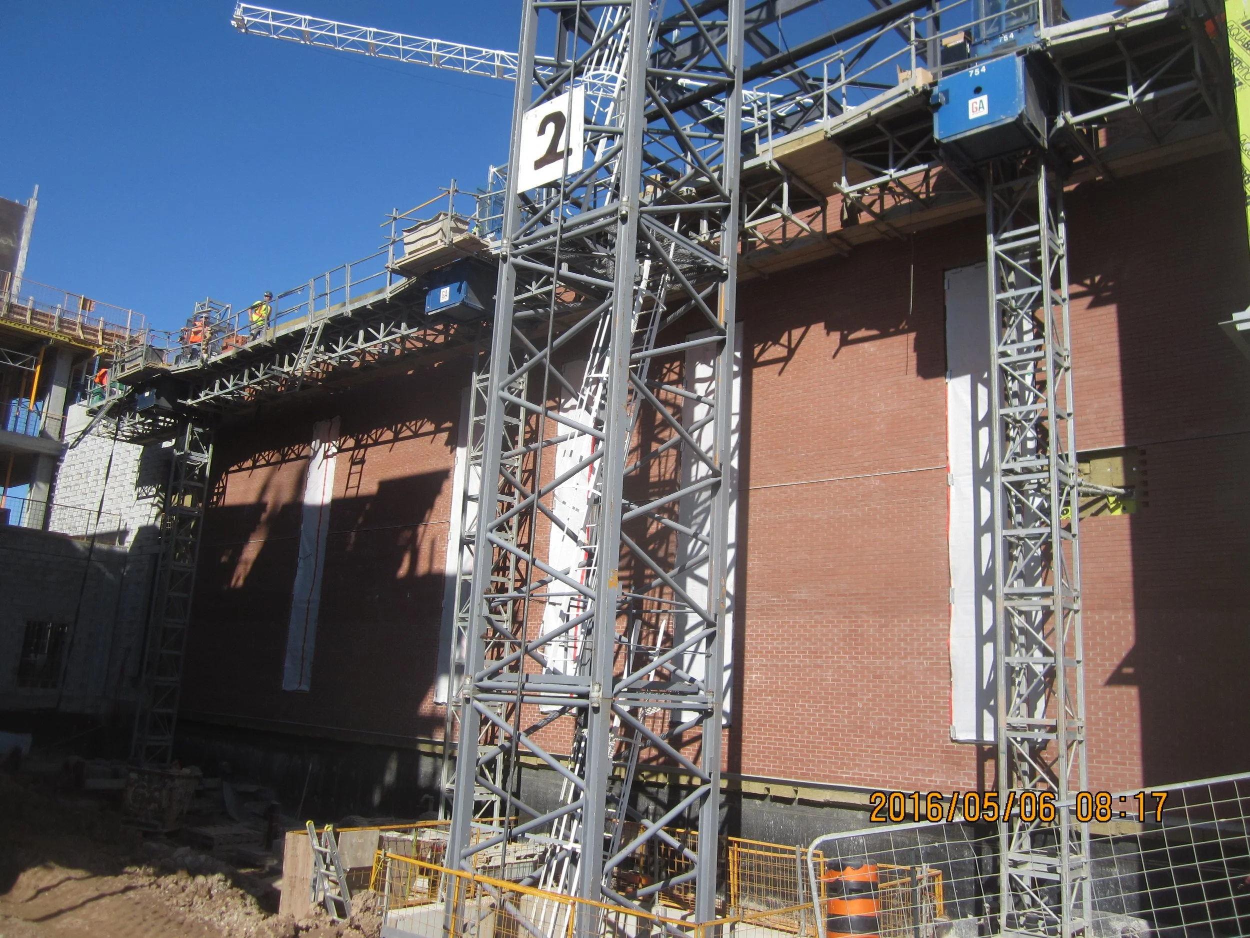 Construction site with scaffolding, workers, and brick wall being built or renovated on a sunny day.