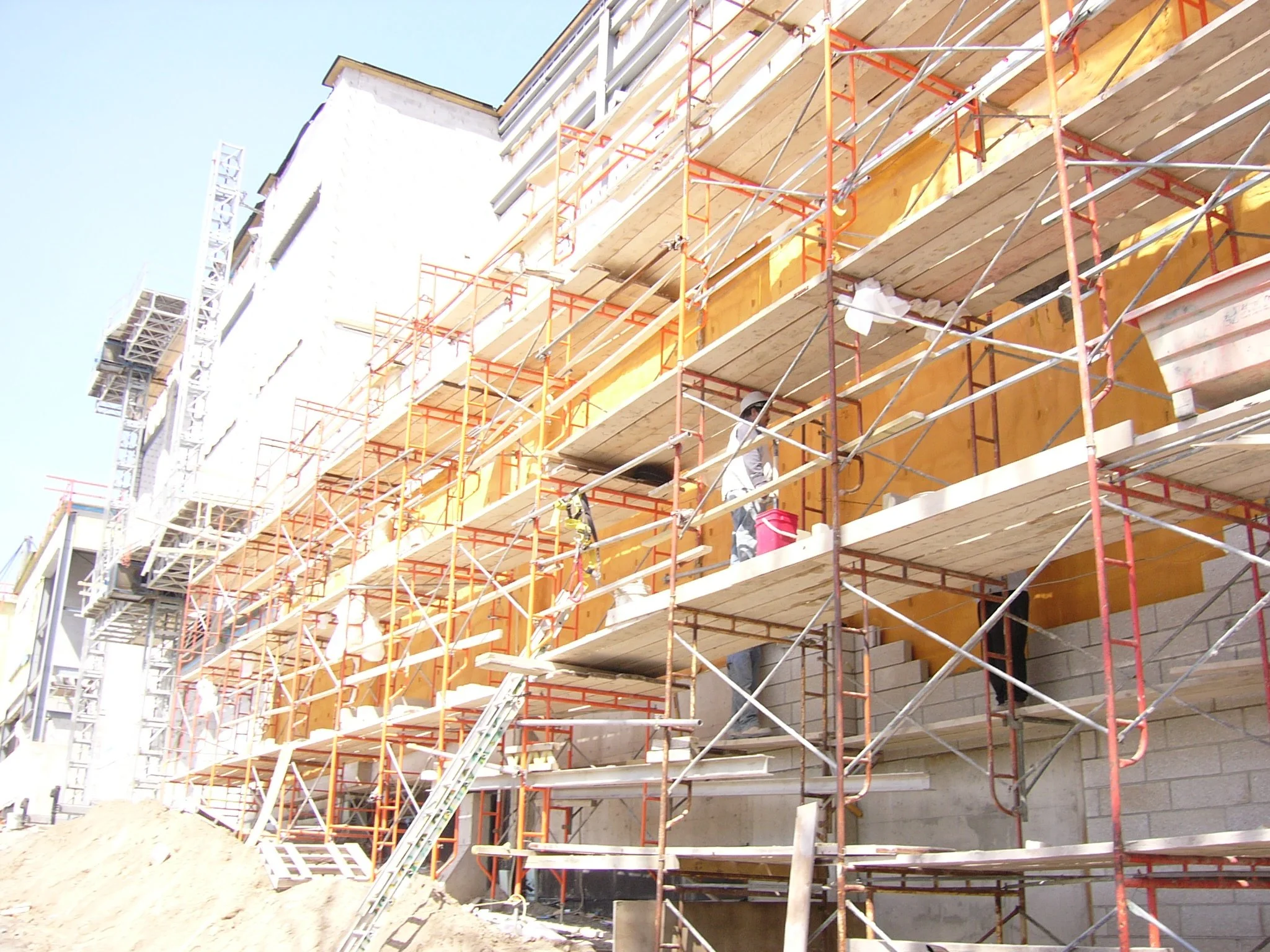 Construction workers building a multi-story building with scaffolding and wooden planks outside under a clear blue sky.