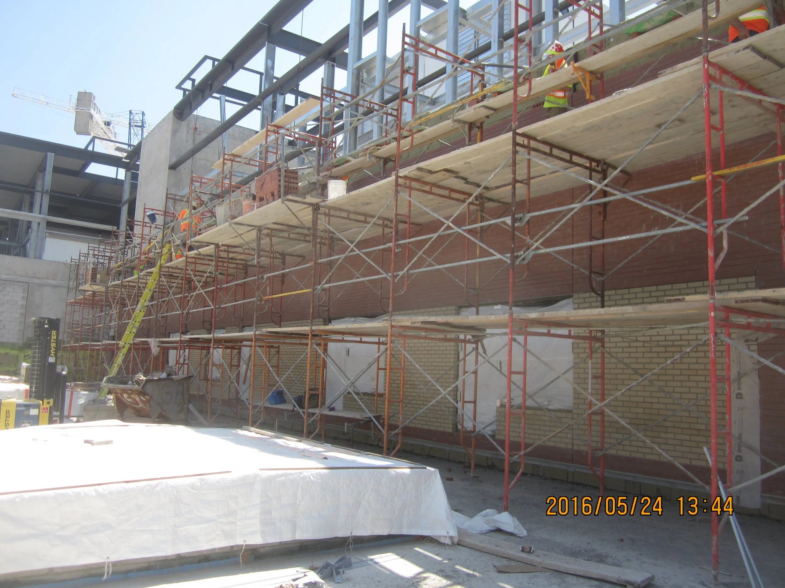 Construction site with scaffolding and workers building a brick wall on a building under construction.