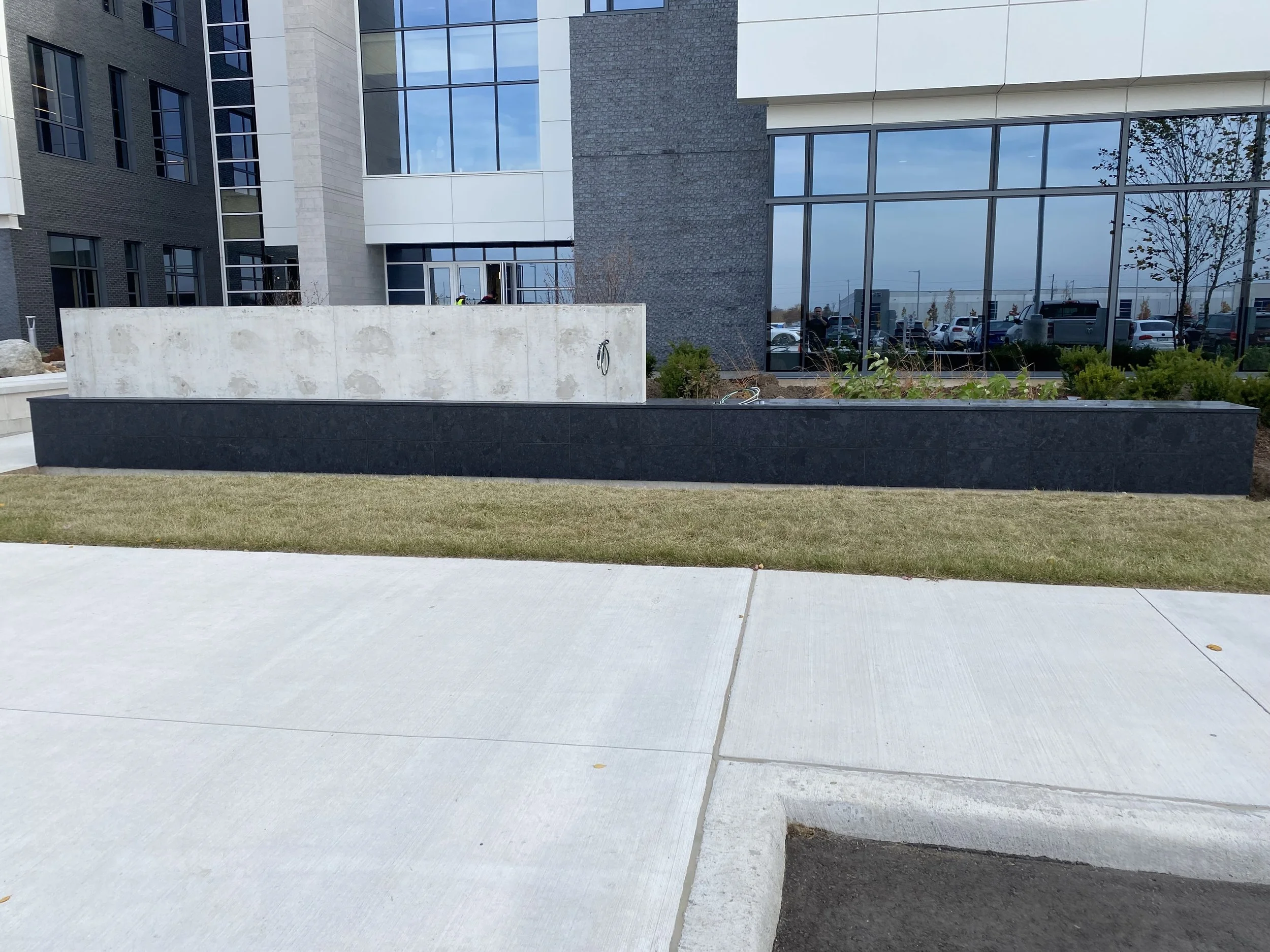 Exterior view of a modern building with large glass windows and a landscaped area with grass and plants.