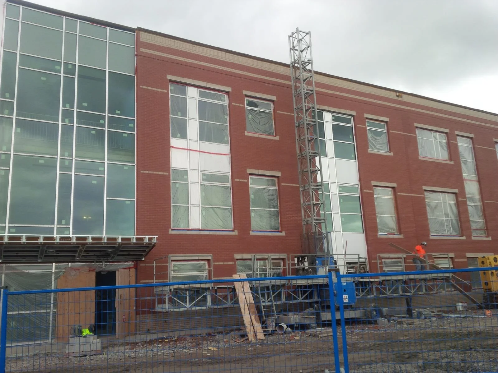 Construction site in front of a brick building with tall windows, scaffolding, and construction workers on site.