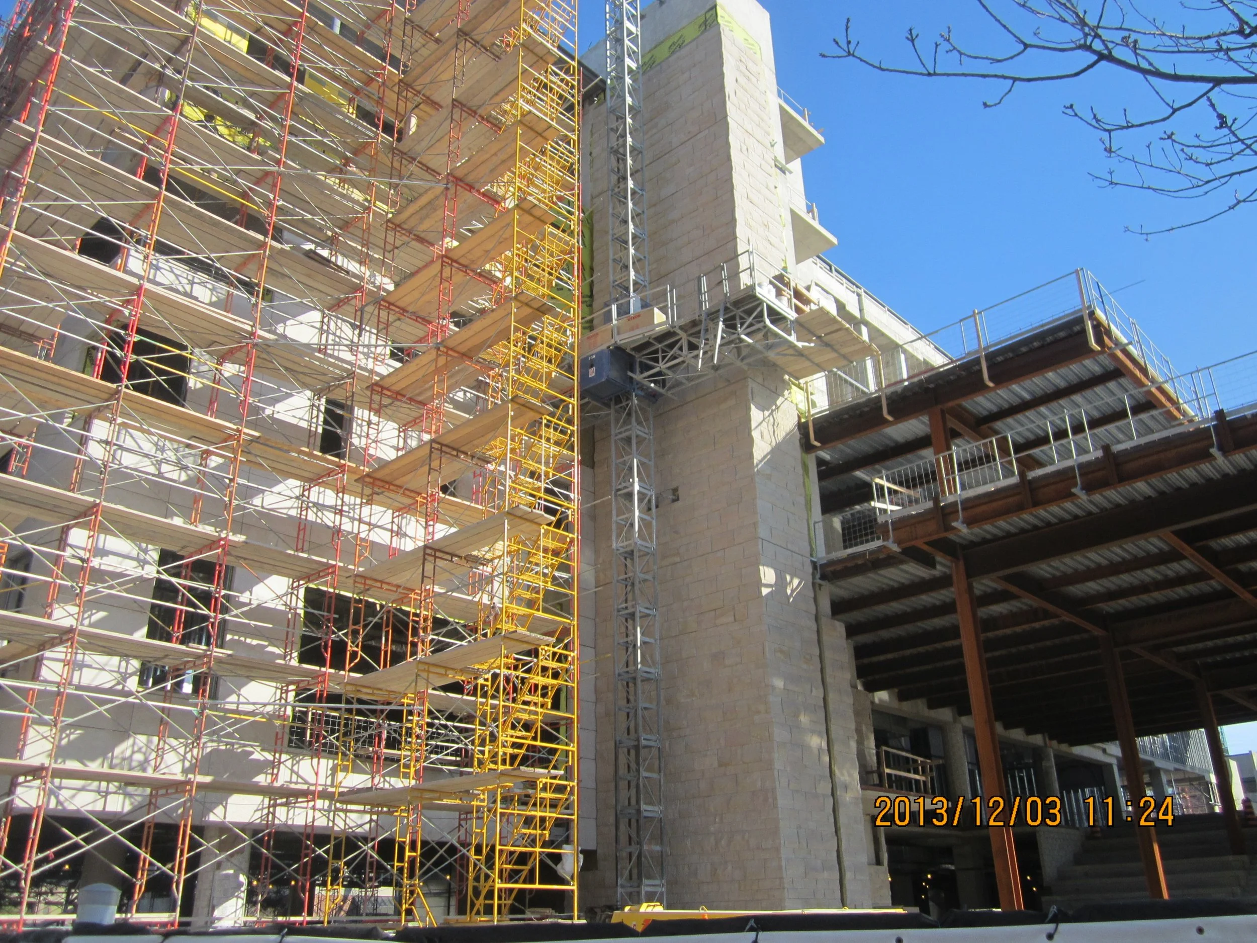 Construction site with scaffolding and a building under construction, showing a stone wall and a partially completed structure with metal framing and platforms.