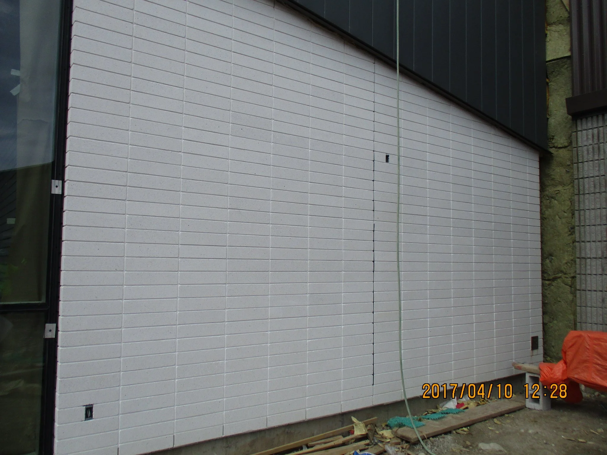 Exterior view of a building wall with white brick siding under construction, with some construction materials and tools on the ground.