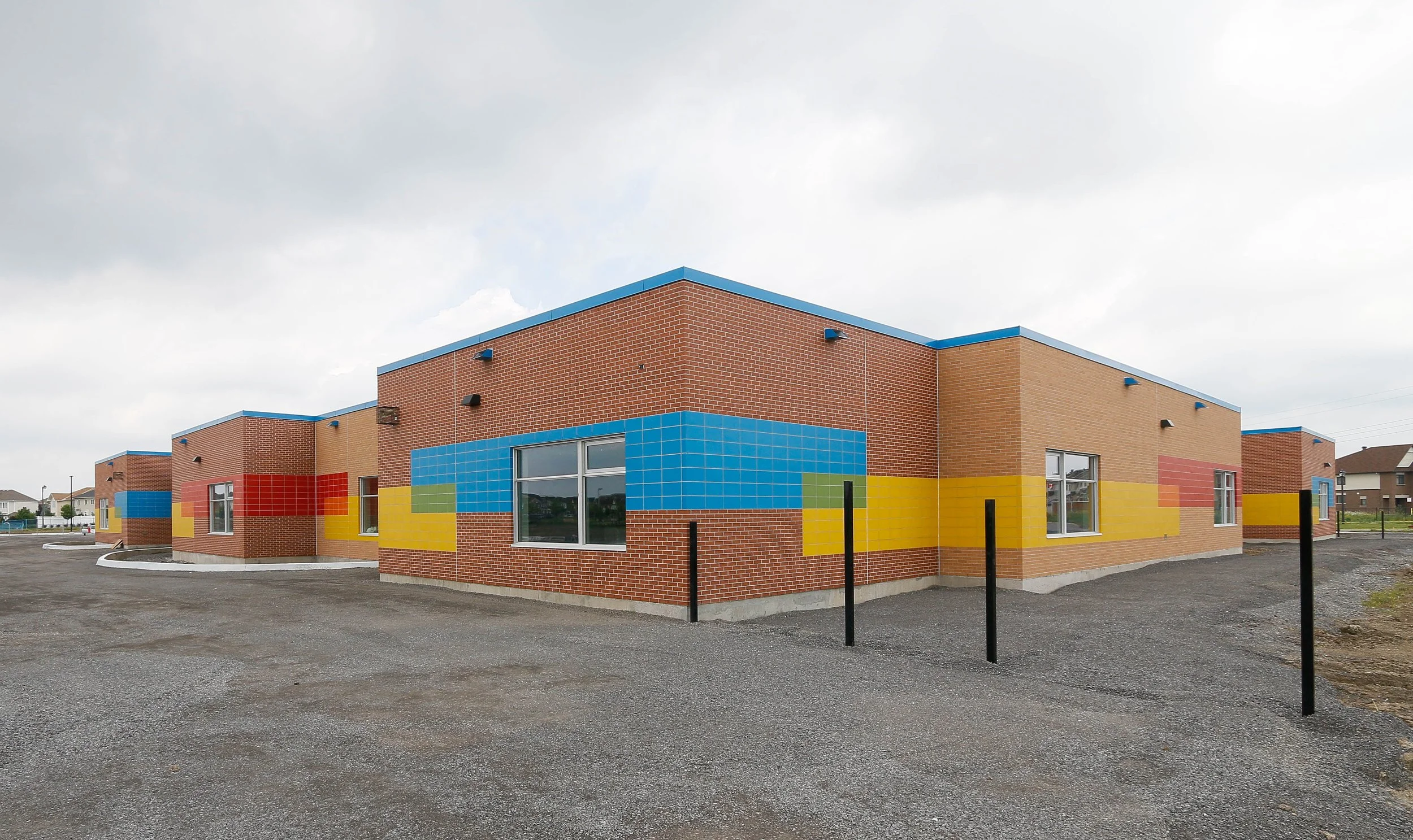 Colorful modern building with brick exterior and blue, yellow, and red tile accents, large windows, and black poles in front.
