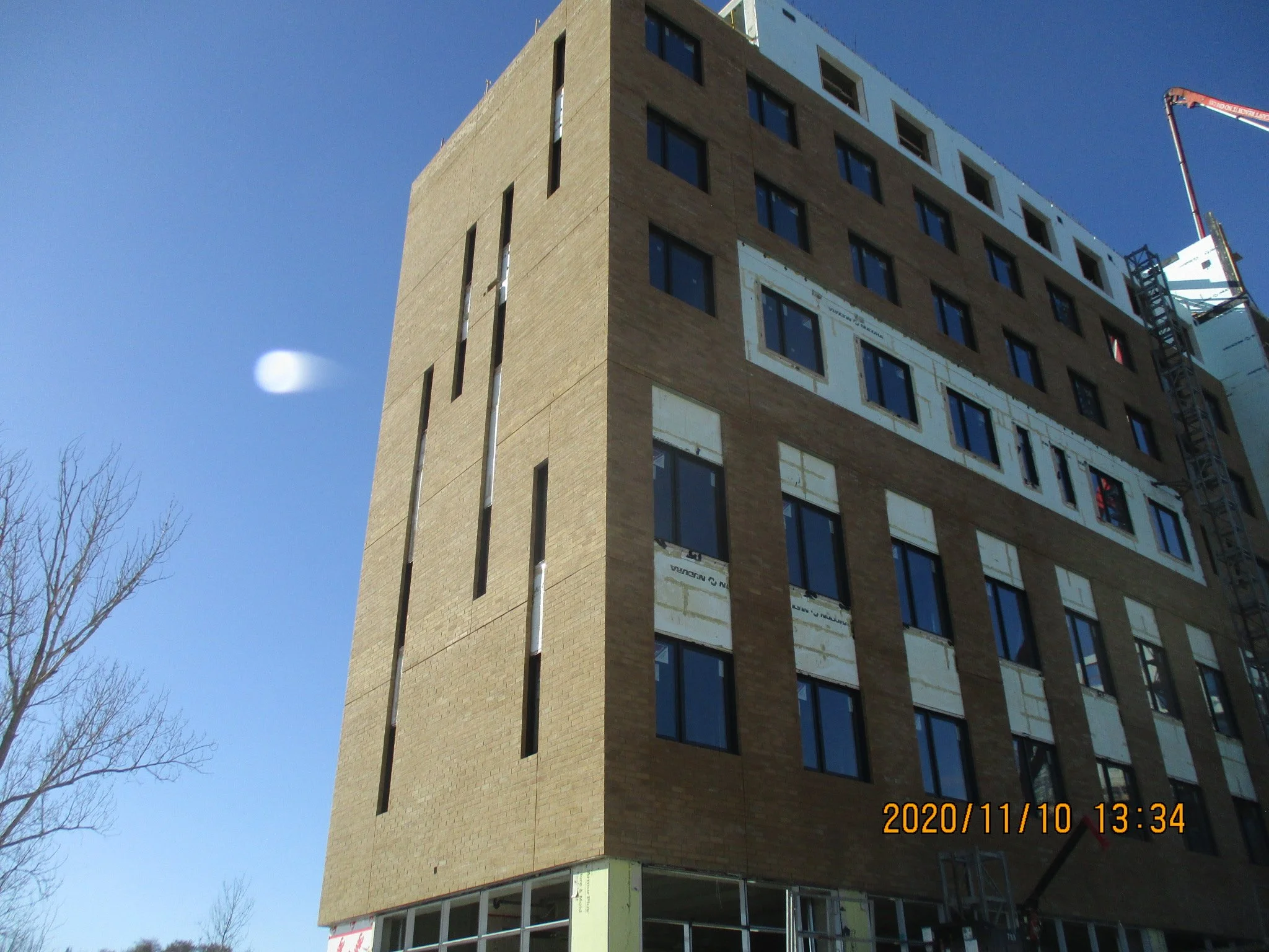 A multi-story building under construction with windows installed, some areas unfinished, and a construction crane on the right side. The sky is clear and blue.