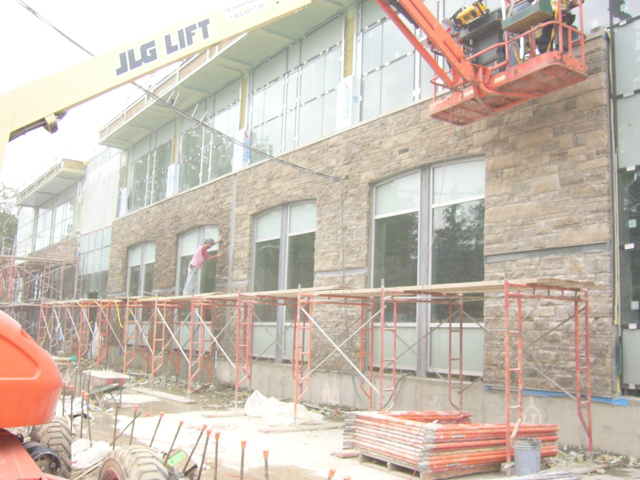 Workers installing exterior stone veneer on a multi-story building with scaffolding and a lift.