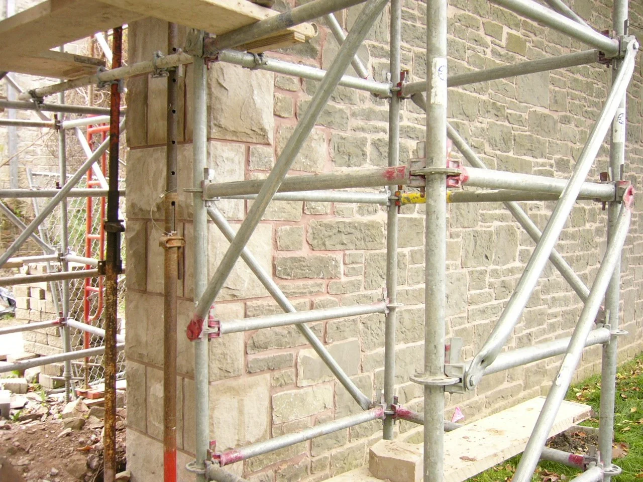 Construction scaffolding and partially built stone wall on a brick building exterior.