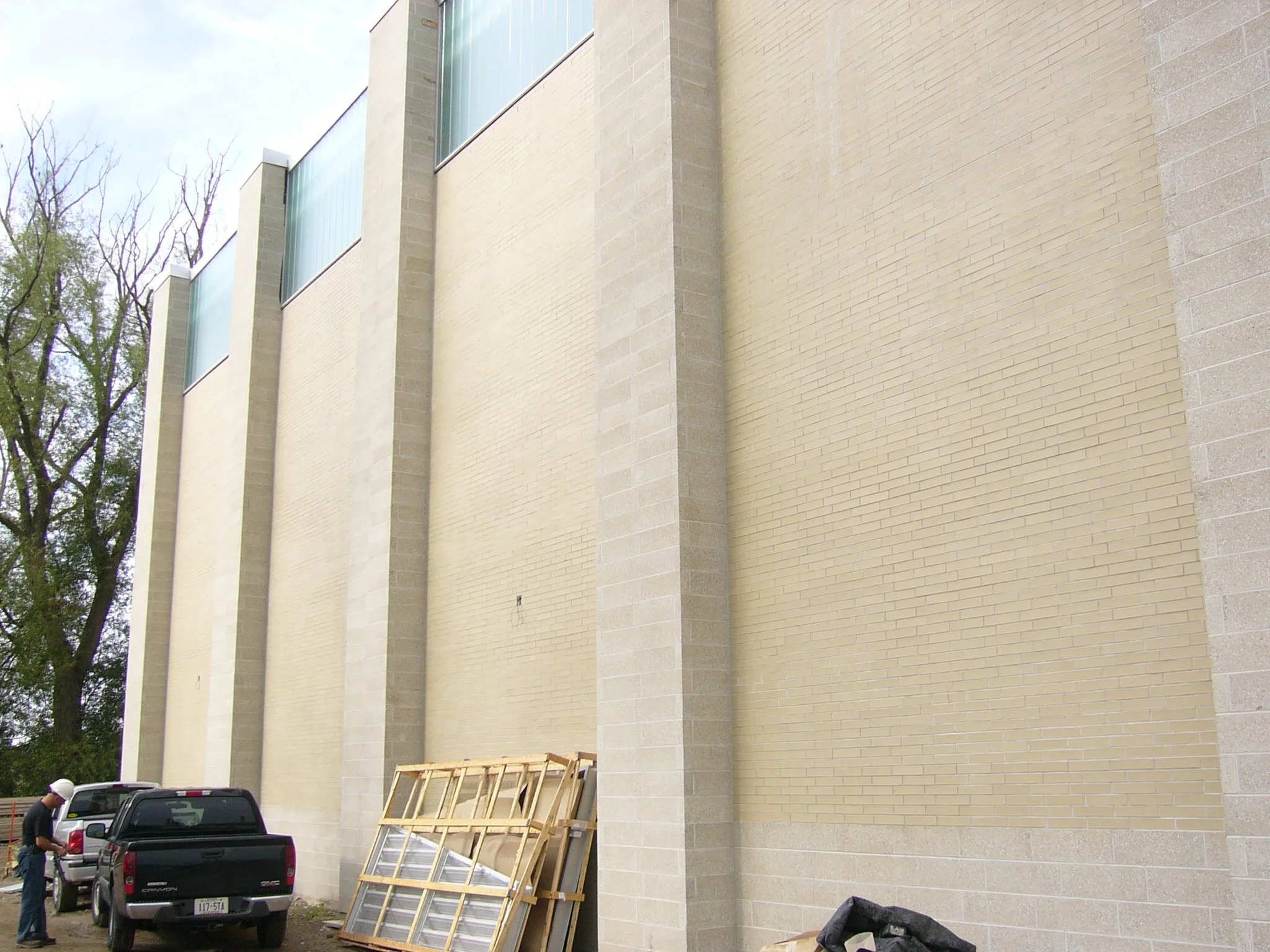 Construction workers and vehicles near a beige brick building undergoing construction or renovation, with scaffolding and building materials present.