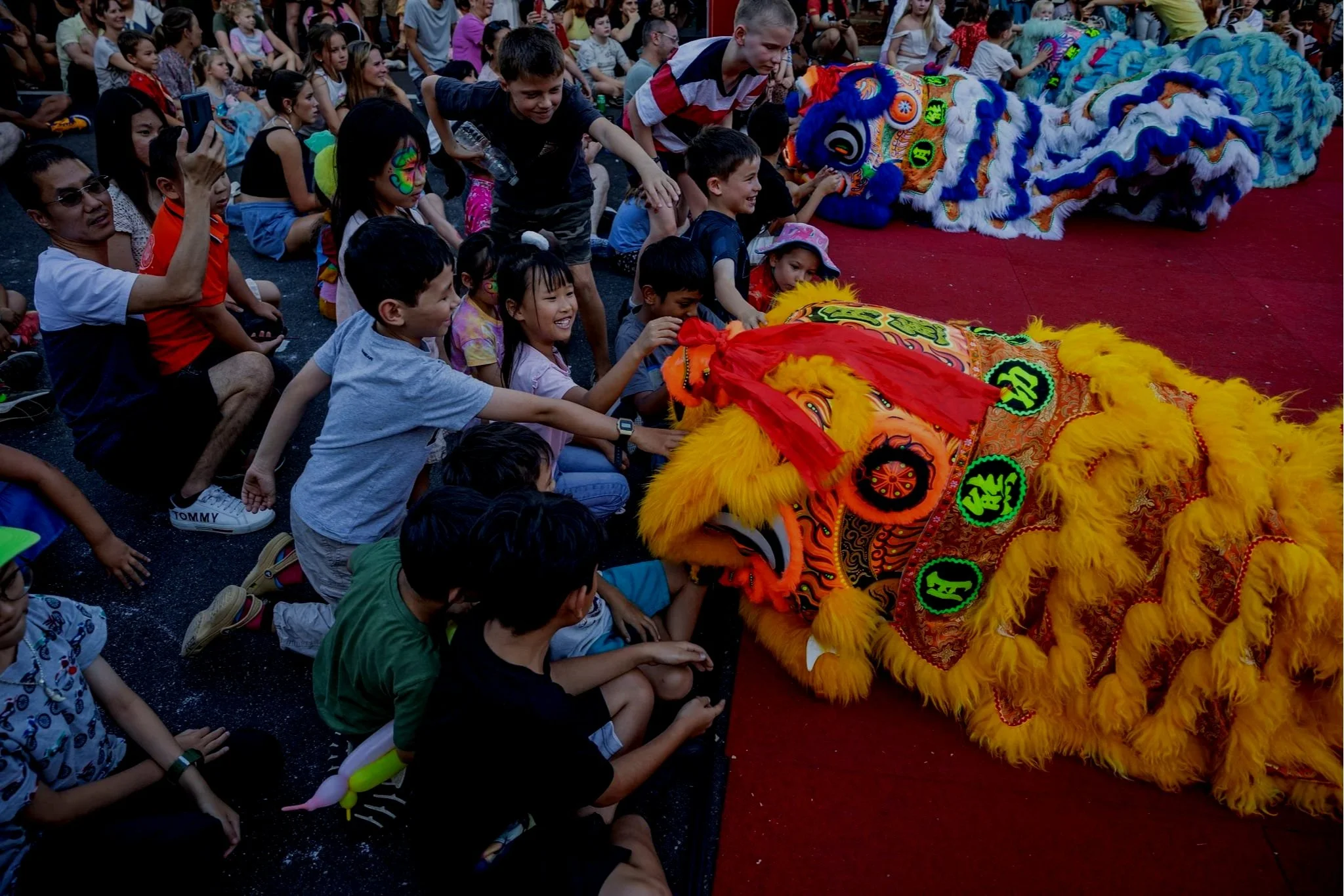 Children watching a Chinese lion dance performance, with some children touching the lion costume.