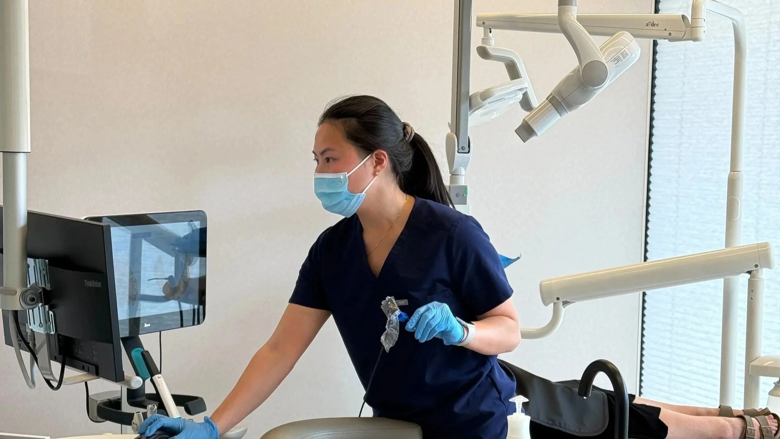 A female healthcare professional wearing a mask and gloves working with dental equipment in a clinic.