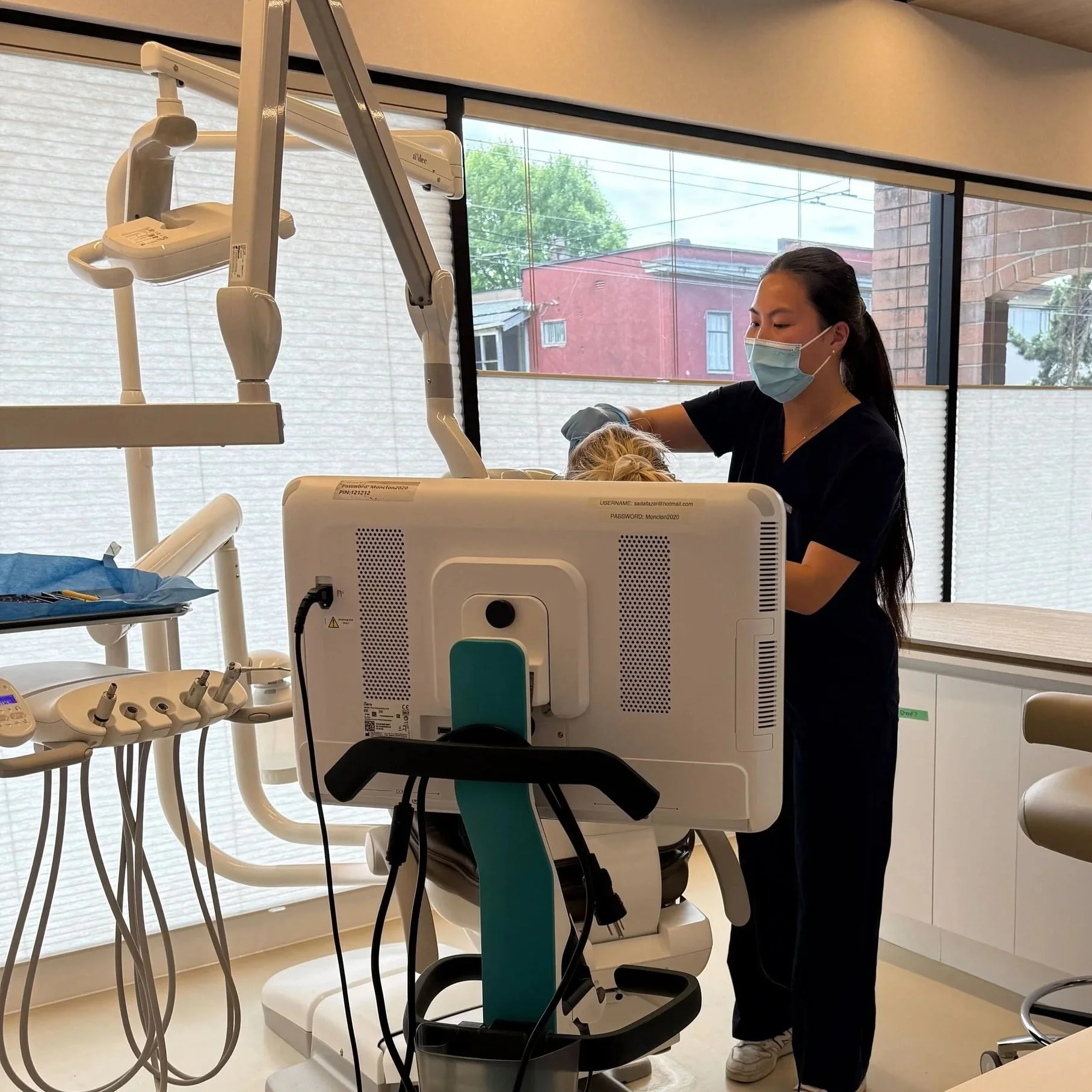 A dental professional wearing a blue face mask and gloves working on a patient in a dental clinic with dental equipment and tools visible.